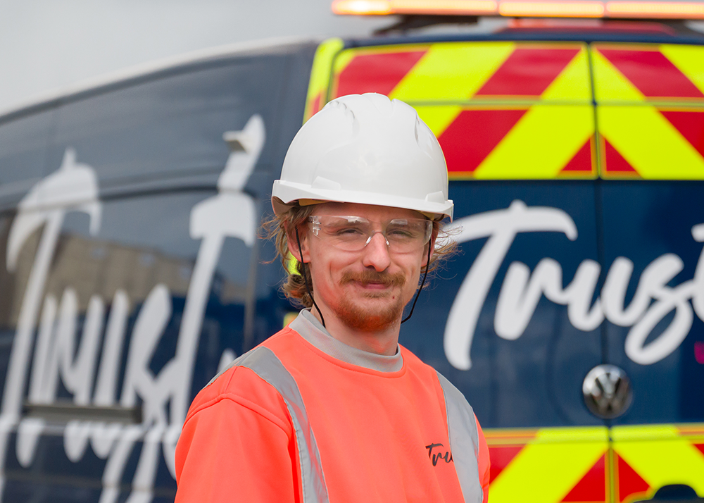 A trust group apprentice in hi-vis workwear infant of a Trust branded blue van.