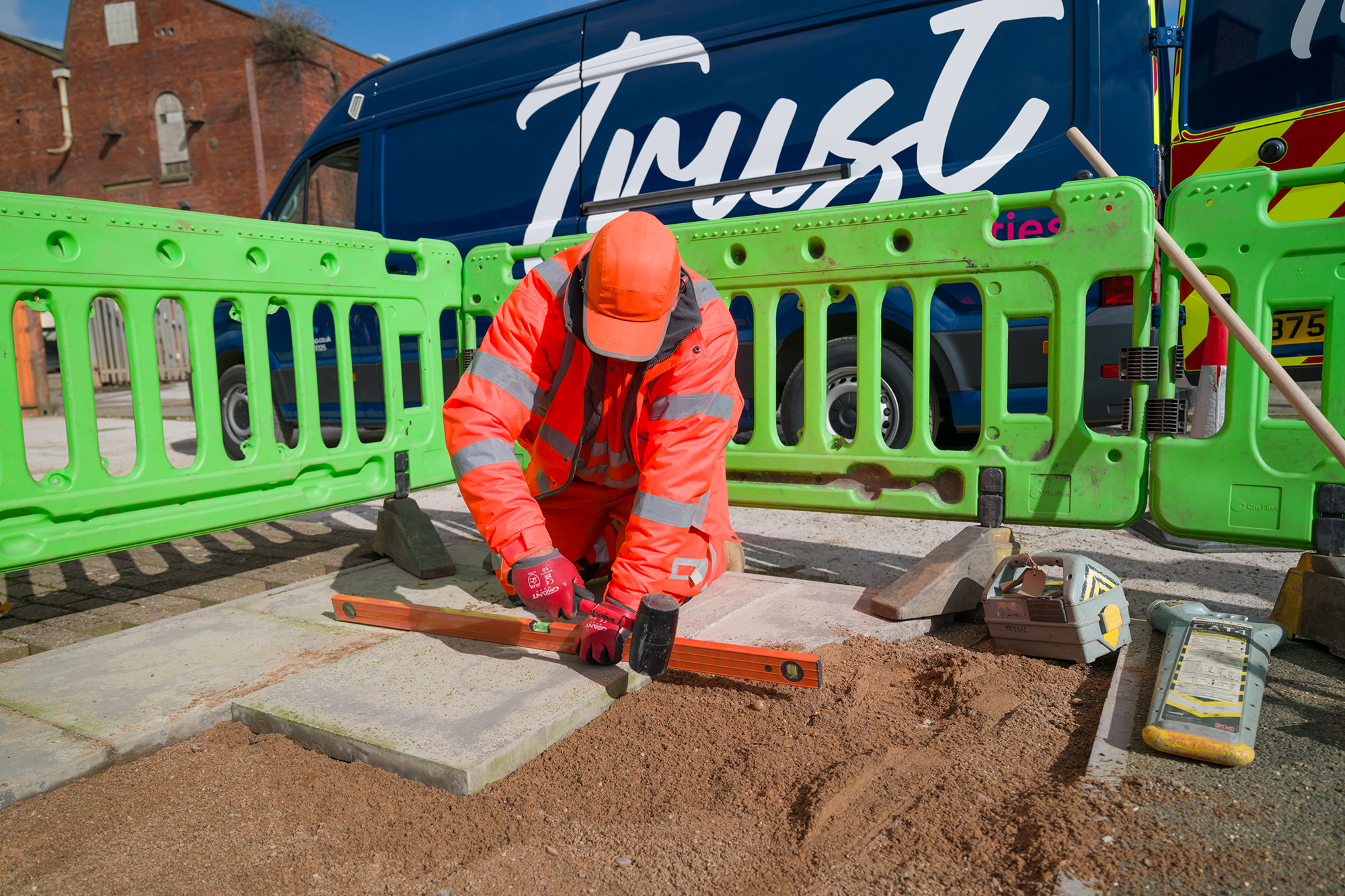 Trust worker in hi-vis clothing reinstating paving slabs one site using hand tools.