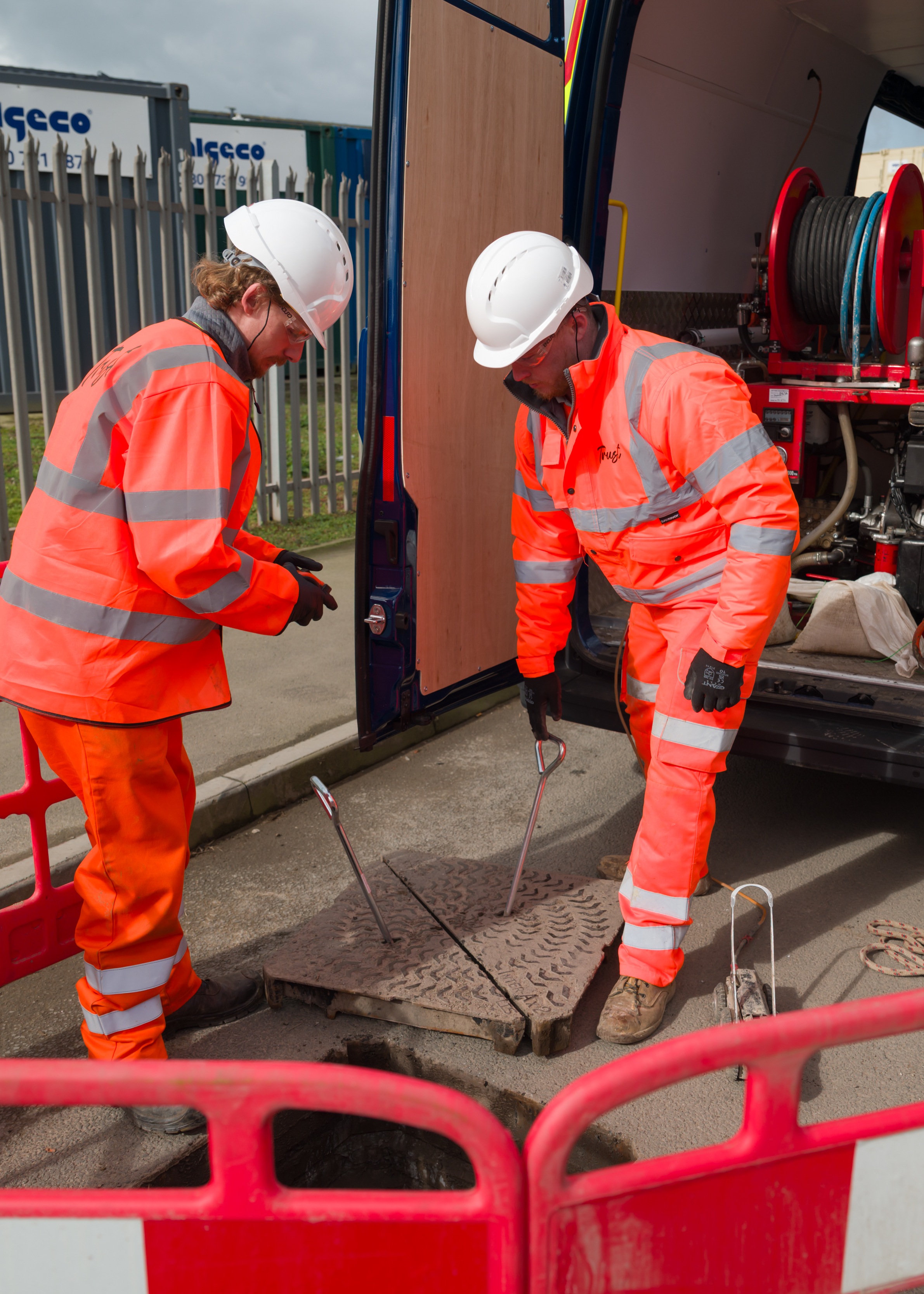 Two Trust workers in hi-vis lifting a man hole cover ahead of a lining job