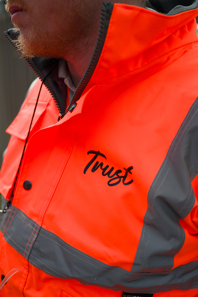 Trust worker in an orange hi-vis branded jacket