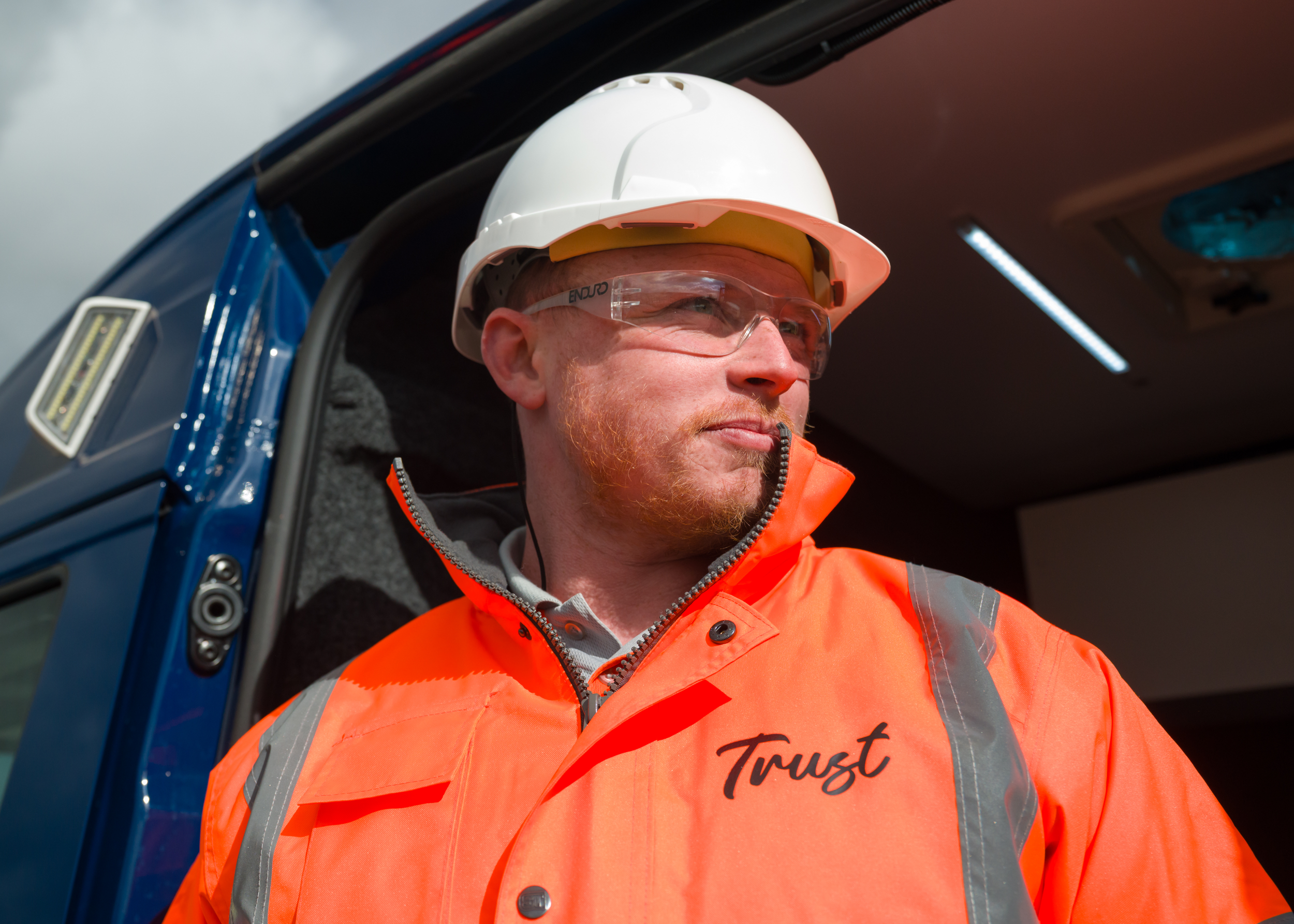 A male worker wearing an orange Trust branded hi-vis jacket and hard hat