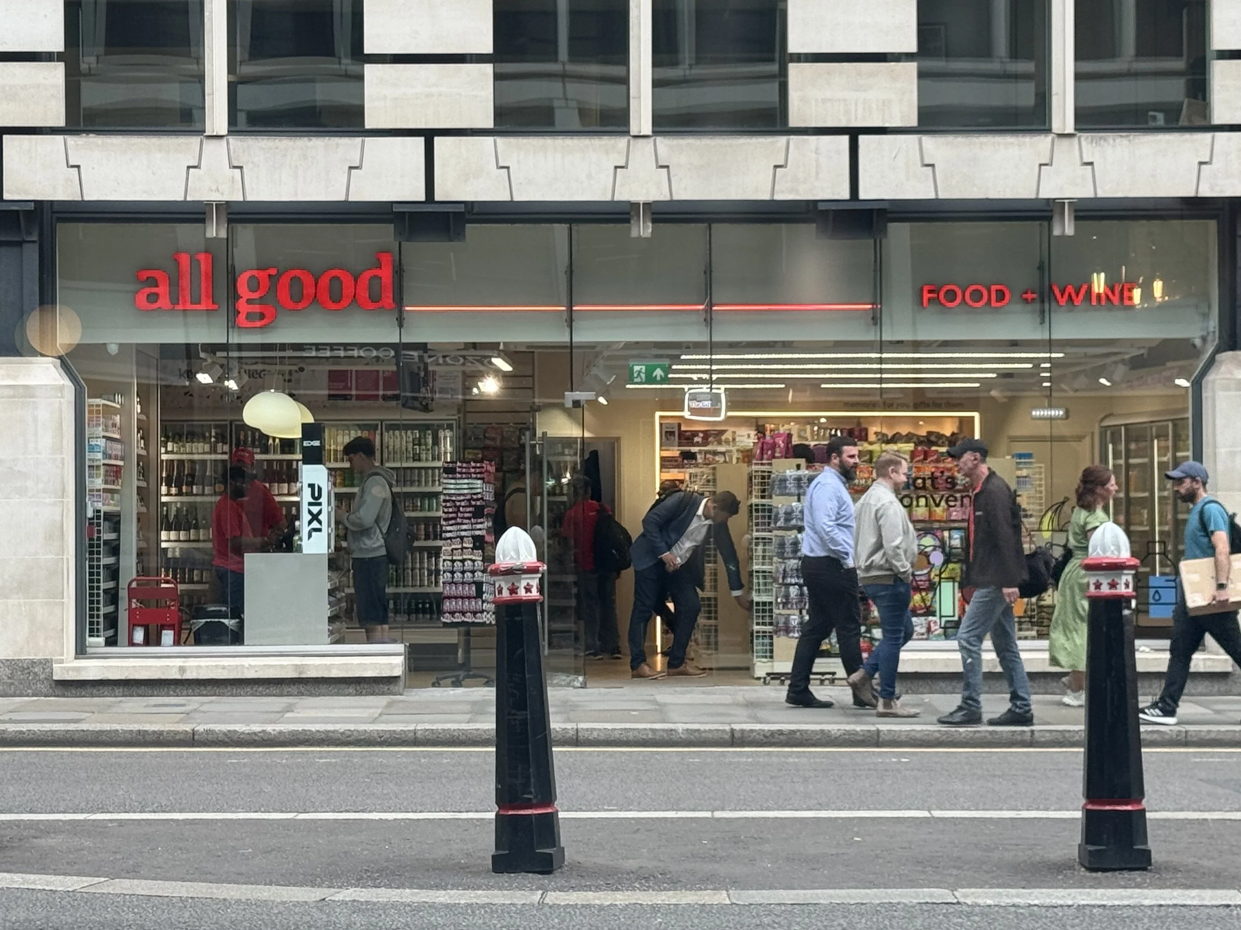 A storefront with a sign that says 'all good' and 'FOOD + WINE' in red letters. People are walking on the sidewalk in front of the store, some looking inside and others passing by.