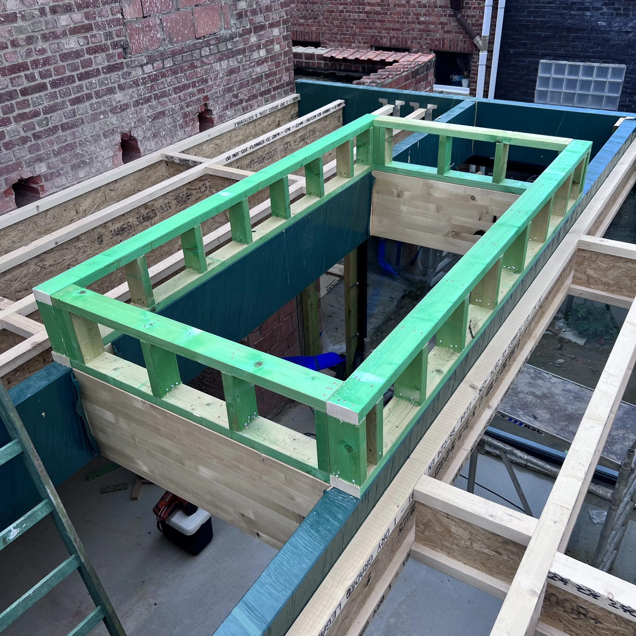 Houten frame voor een koepel, met groen geverfd hout en een ladder op de voorgrond.