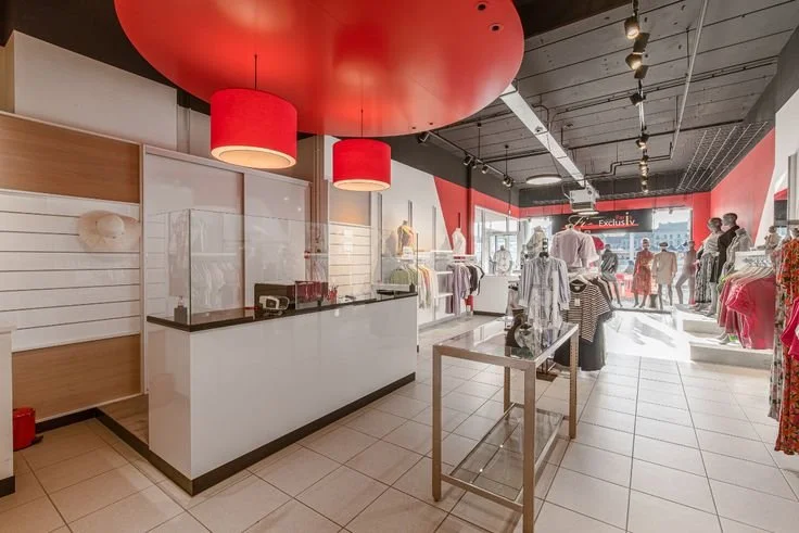 Beeld voor de verbouwingen - binnen in een kledingwinkel met witte tegels, vitrines, paspoppen en rode plafonddecoratie.