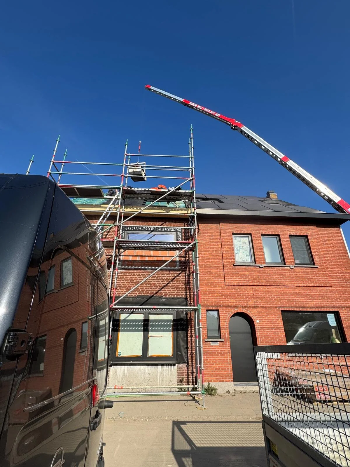 Stellingen en een kraan staan opgesteld naast een rood bakstenen gebouw op een zonnige dag.