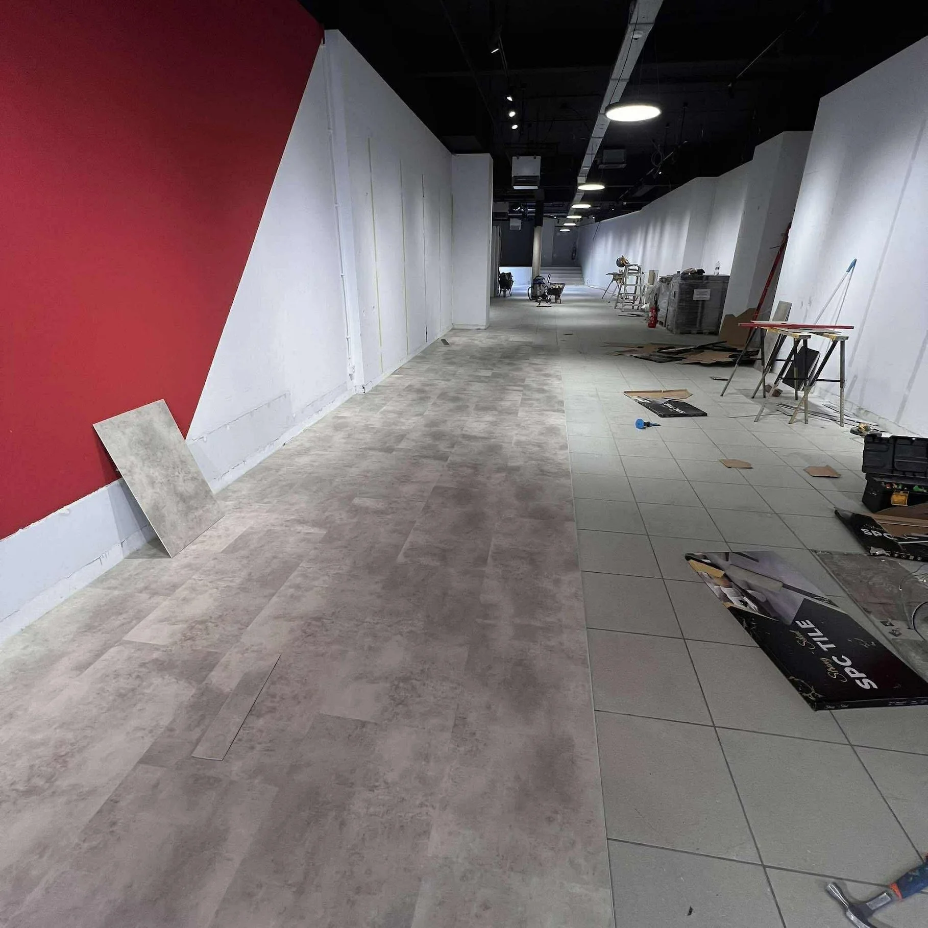 Interieur van een winkel in renovatie, met onafgewerkte vloeren, bouwmaterialen, gereedschap en meubels verspreid over de gang.