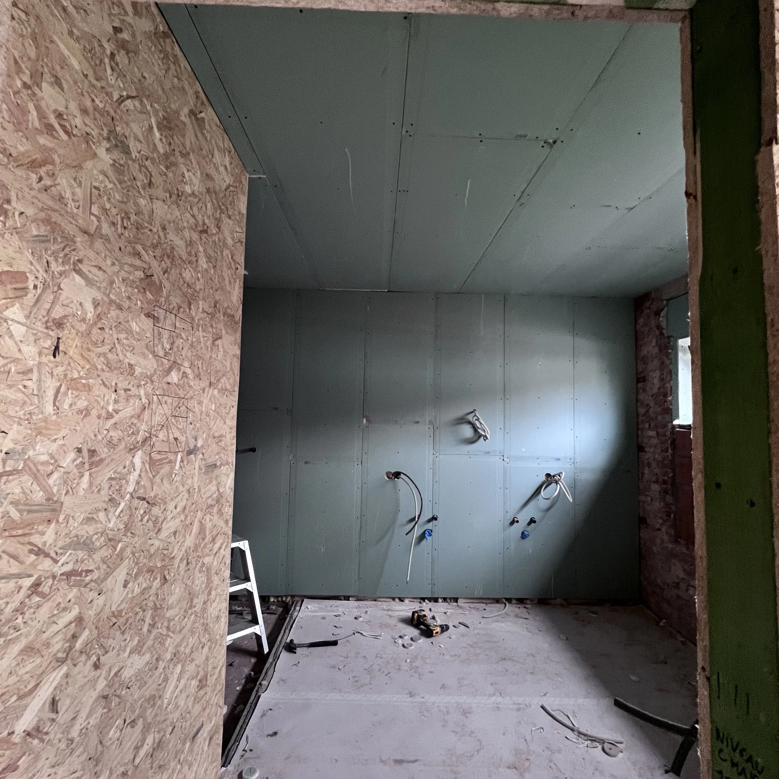 Interieurfoto van een ruimte in aanbouw met gipsplaatinstallatie, elektrische bedrading die aan de muur hangt en gereedschap op de vloer.