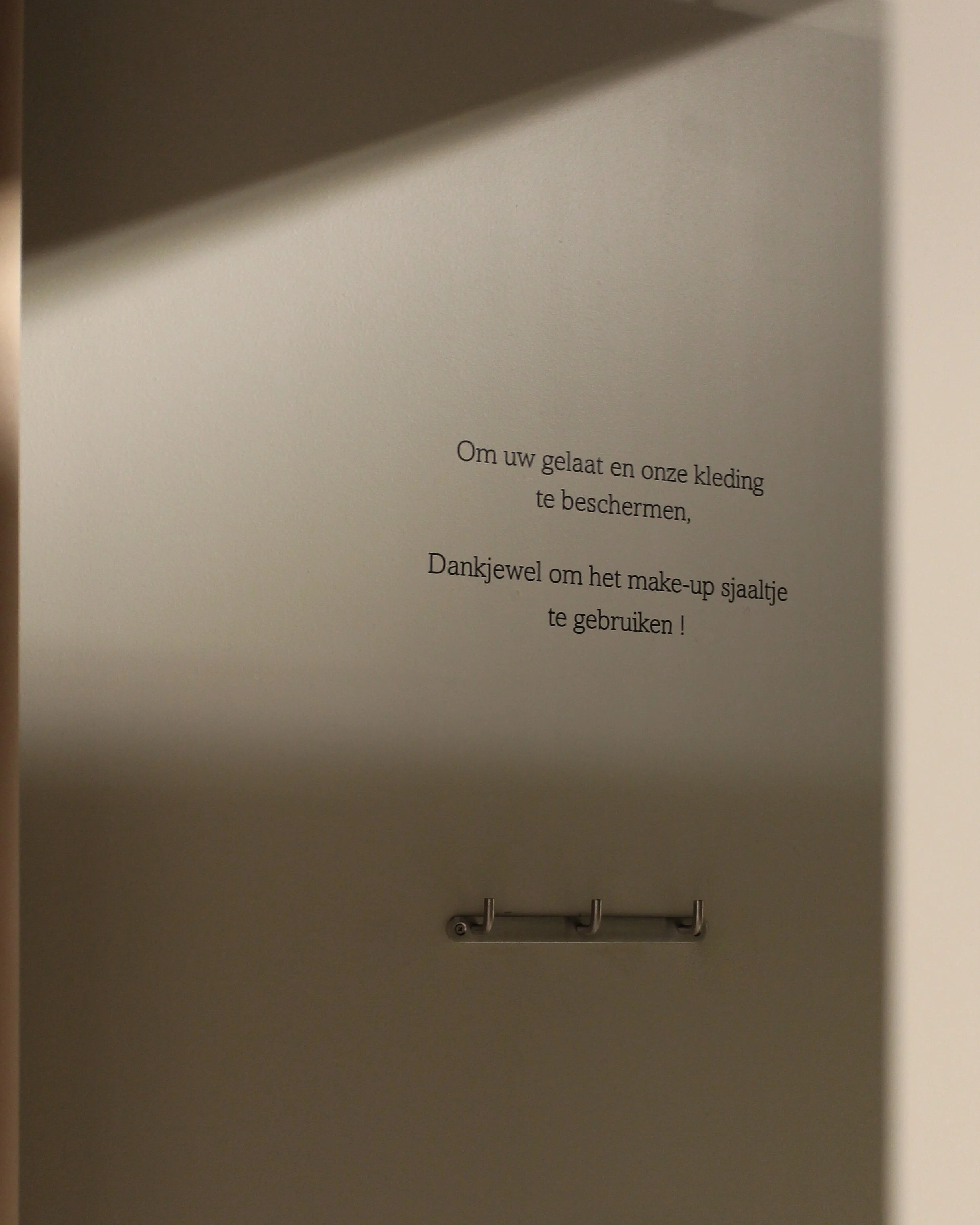 Een tekst aan de muur van de paskamer waarin bedankt wordt voor het gebruik van make-up- en kledingbeschermers.