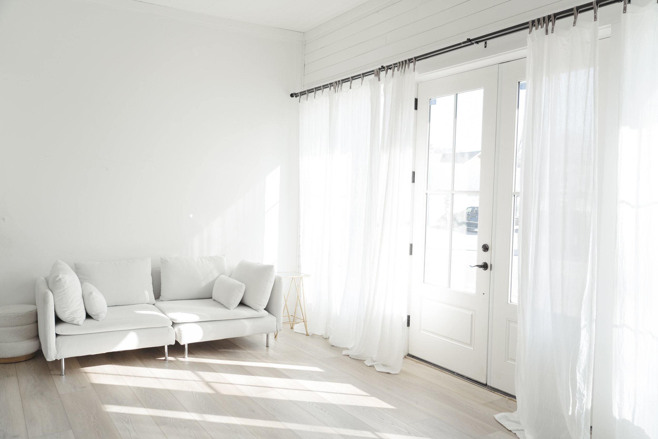 Bright living room with white sofa, sheer white curtains, and white walls.