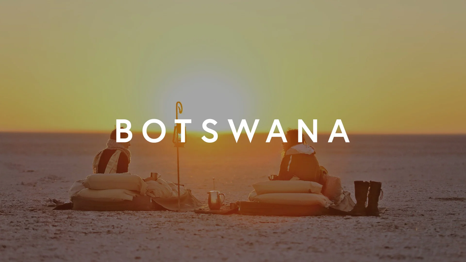 Two people sitting on the ground with pillows and blankets at sunset in Botswana, Africa.