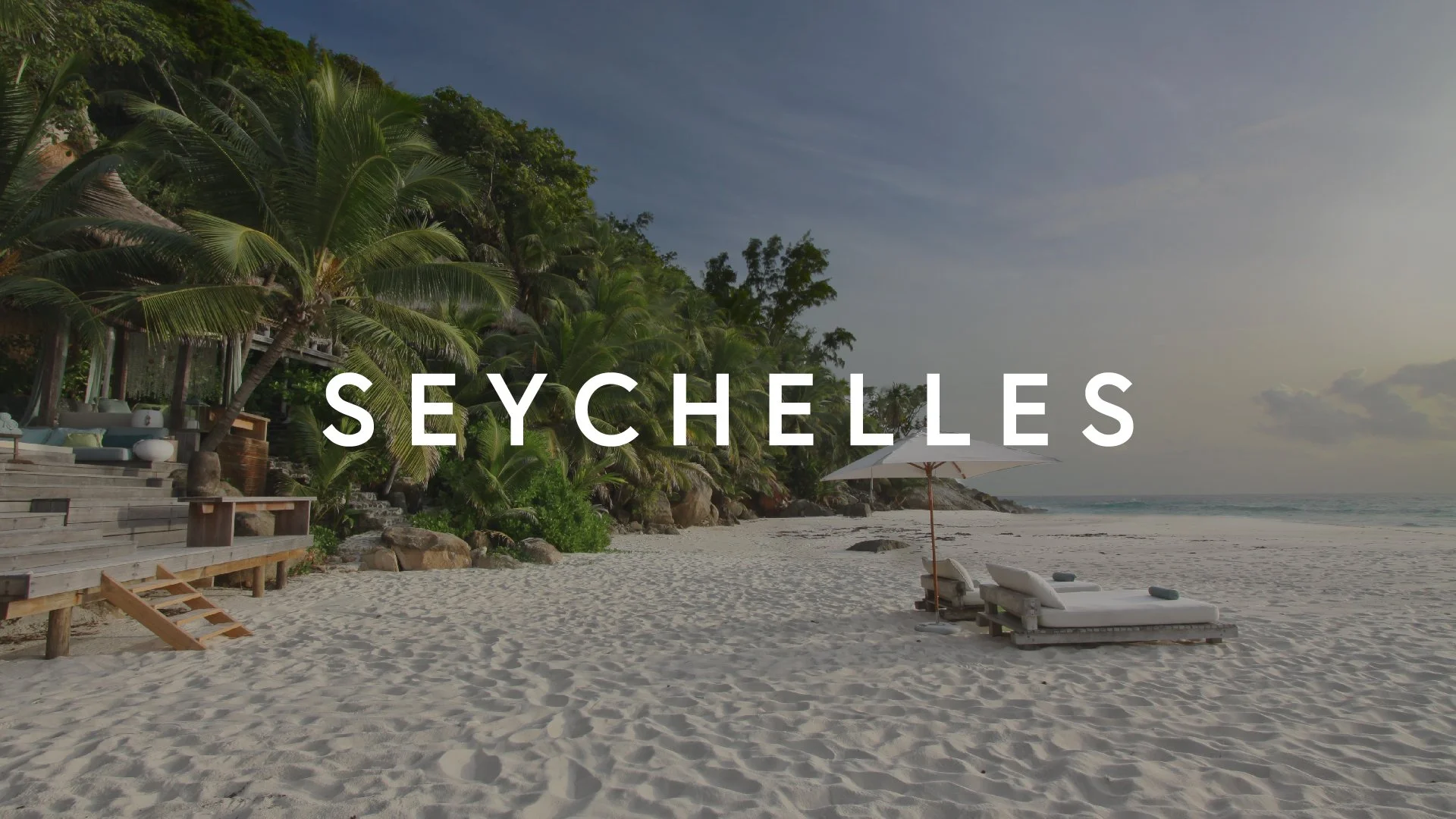 Seychelles beach with palm trees, lounge chairs under umbrella, and ocean view