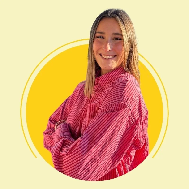 Jeune femme souriante portant une chemise à rayures rouges, avec les bras croisés devant un fond jaune avec un cercle blanc.