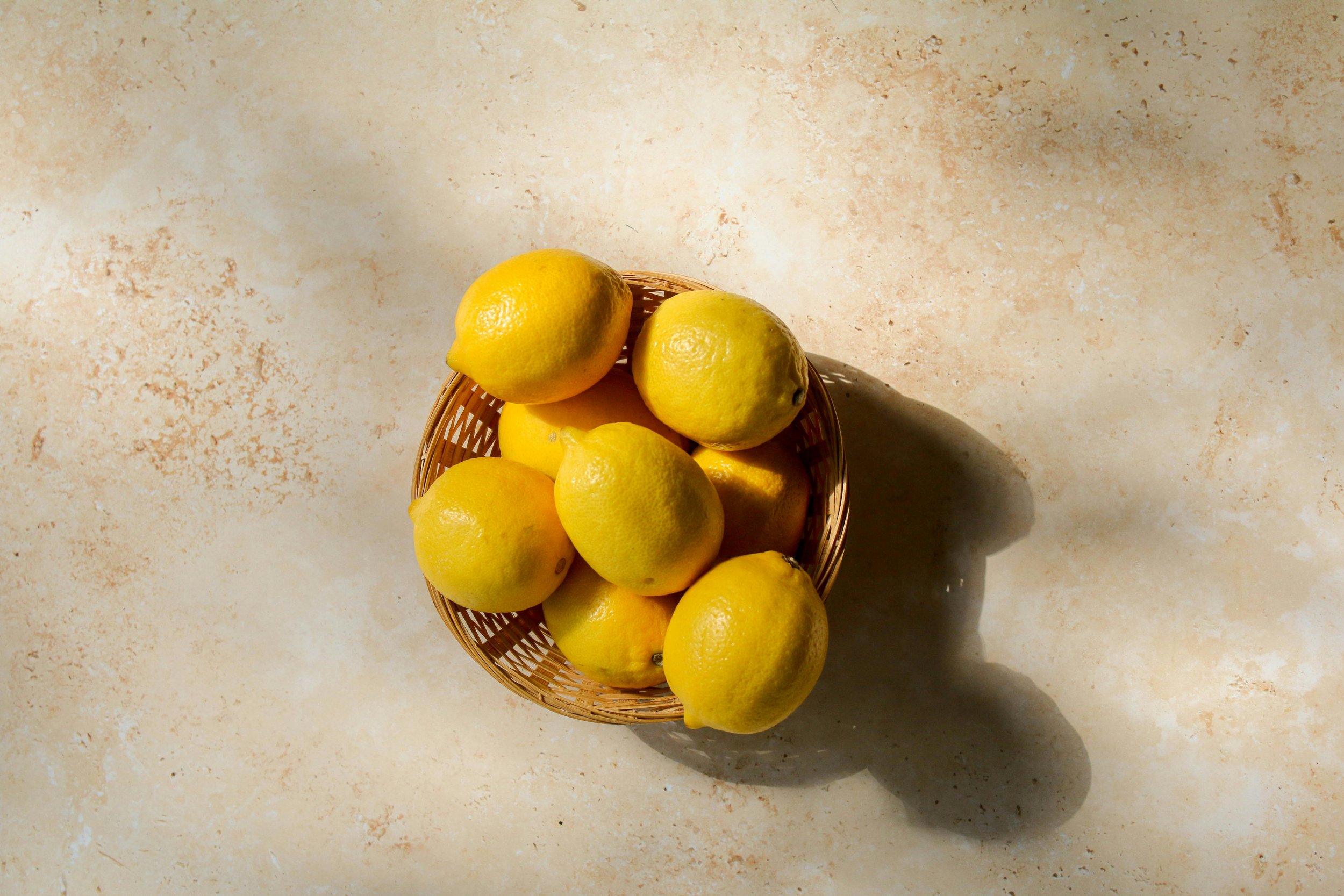 Un panier en osier contenant des citrons jaunes sur une surface beige, vue de dessus.