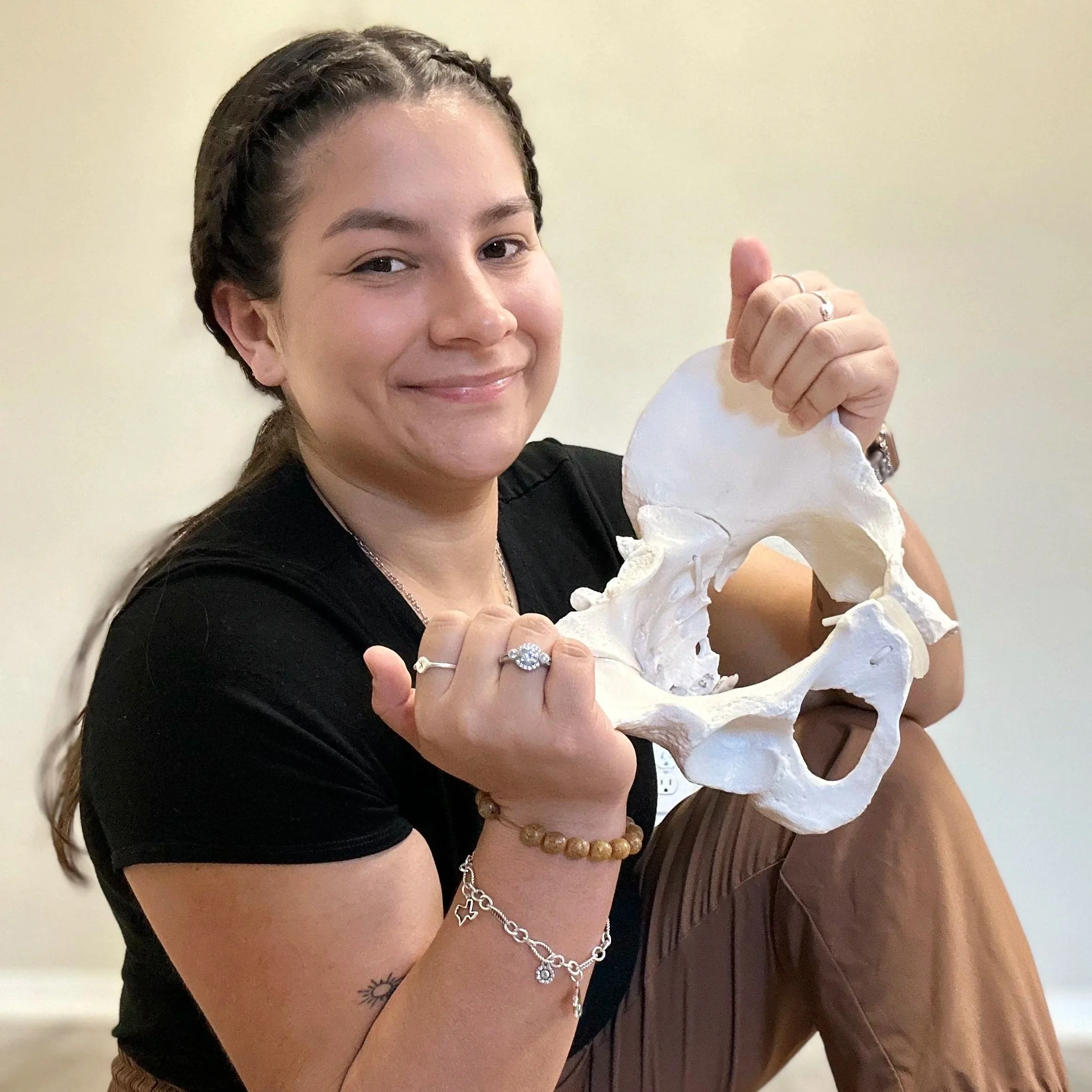 Krissa the Doula sitting on the floor holding a pelvic model used for childbirth education, supporting informed decision-making as a birth doula serving Central Texas families