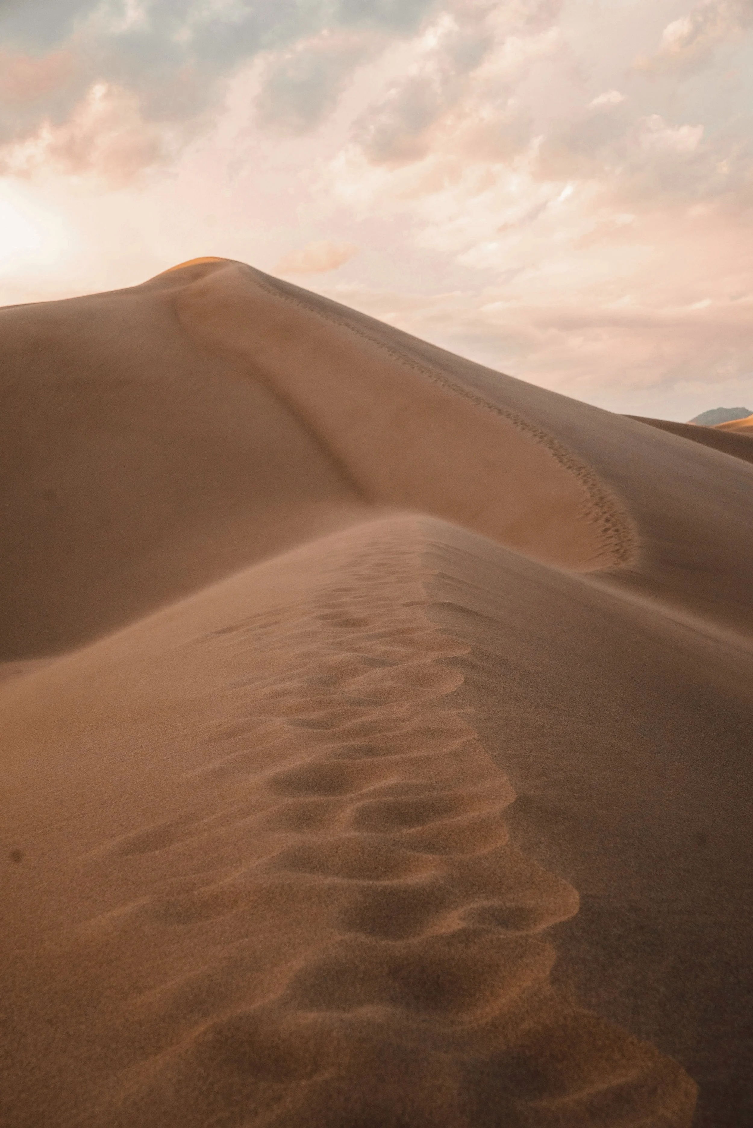Sand dunes with footprints on a cloudy sky at sunset.