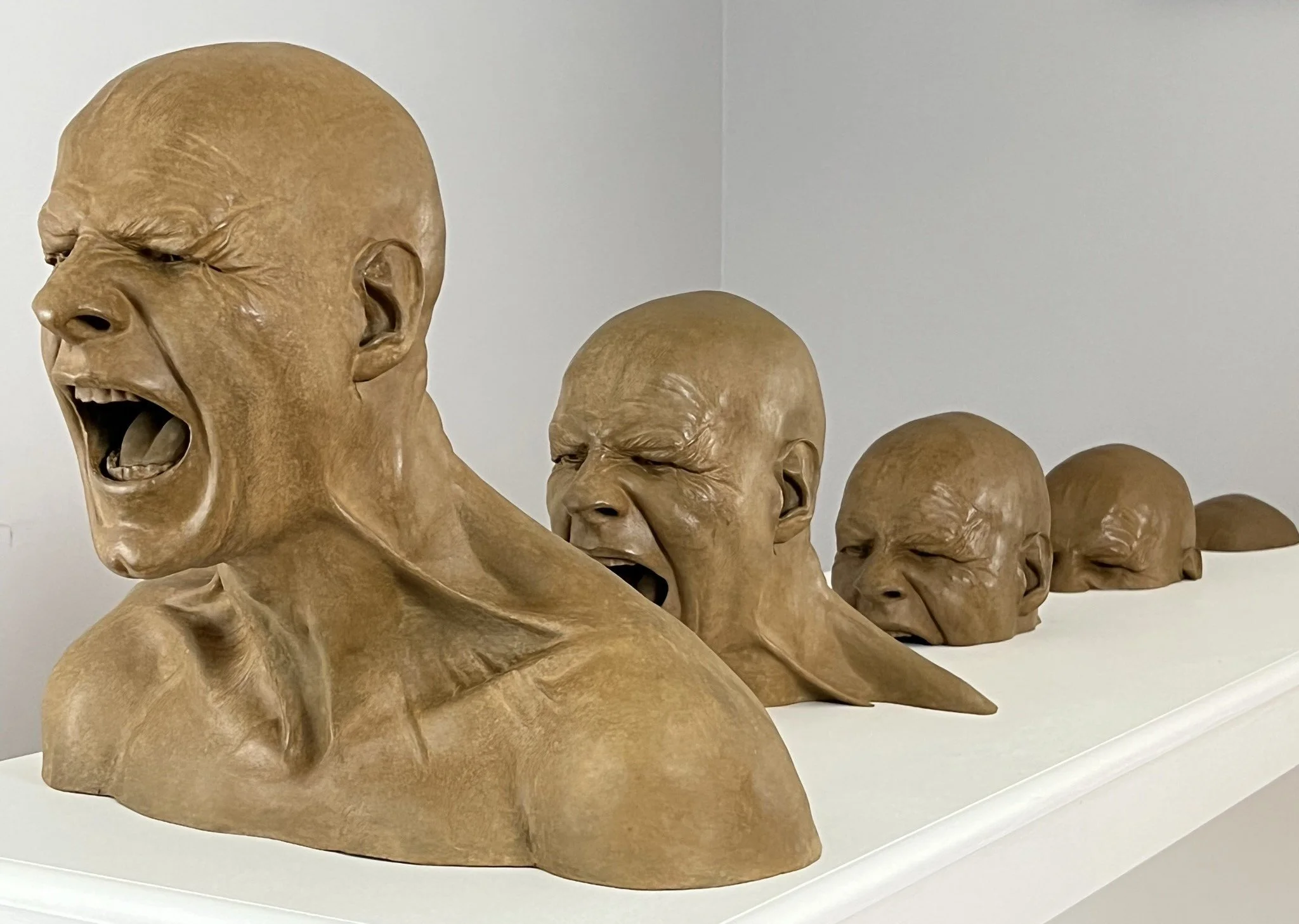 Bronze sculpture of angry men rising up from a surface