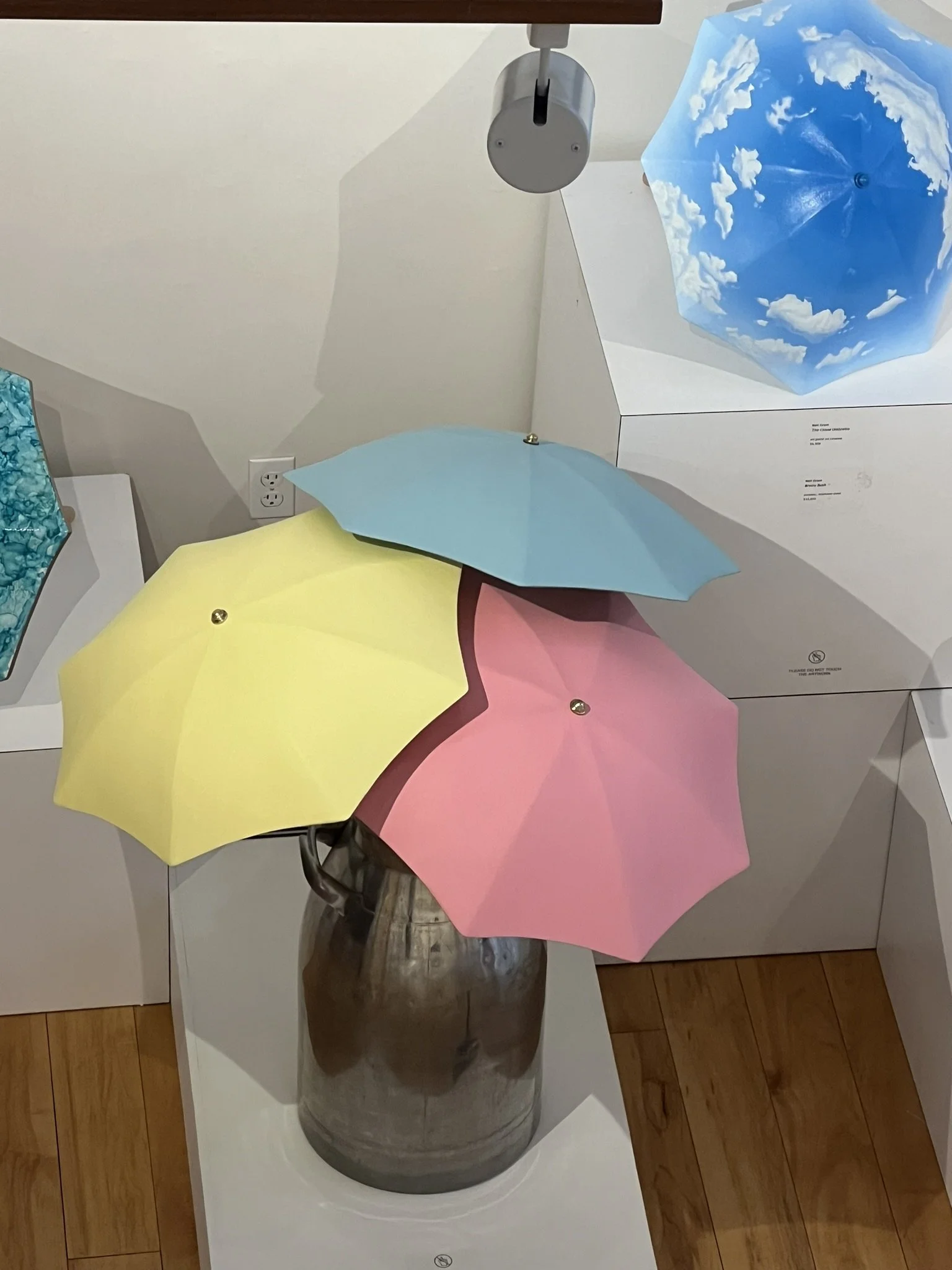 Collection of three large umbrellas painted in yellow, pink and baby blue sitting in a steel milk urn