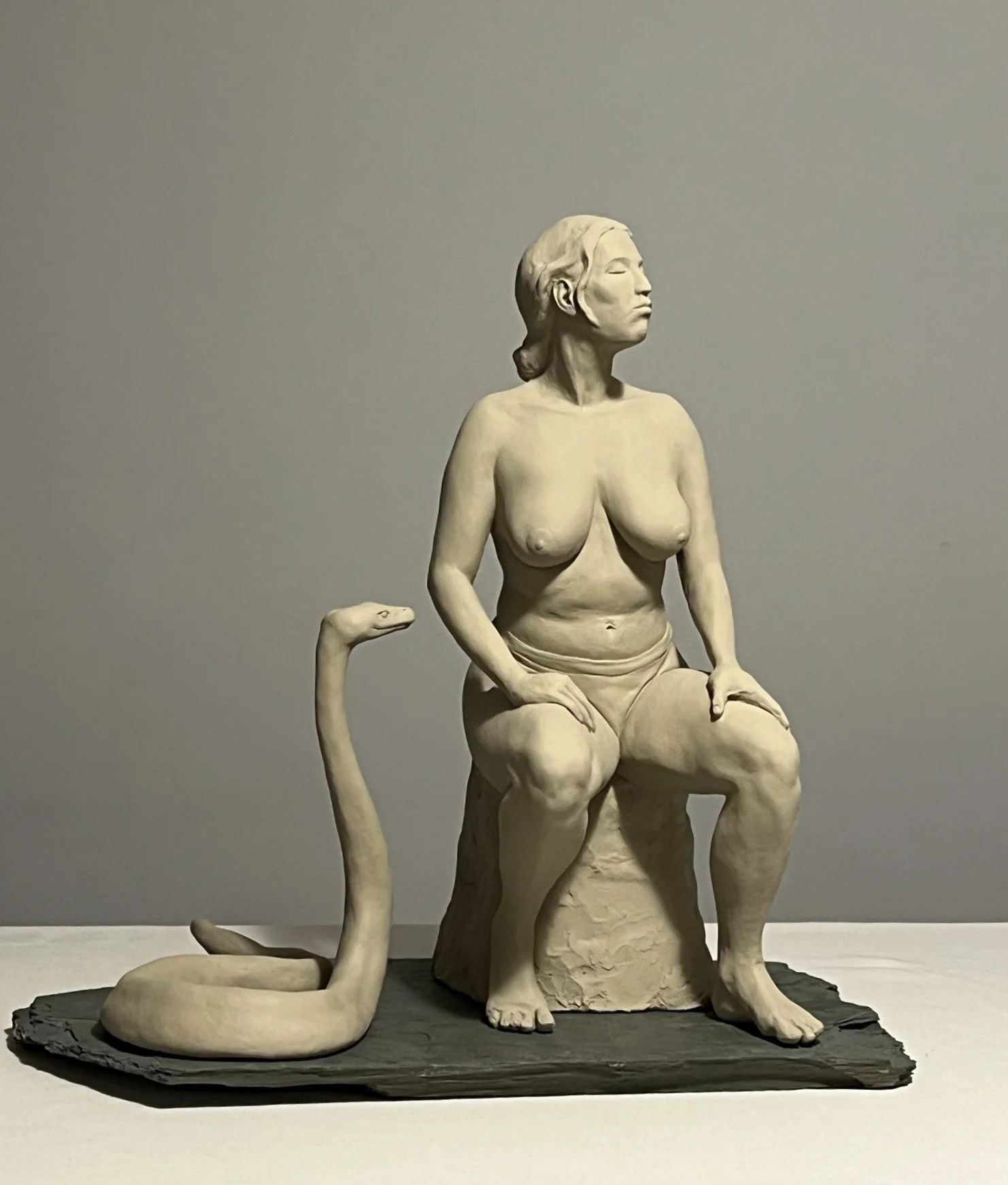 A seated bare-chested woman turning away from a conspiratorial python