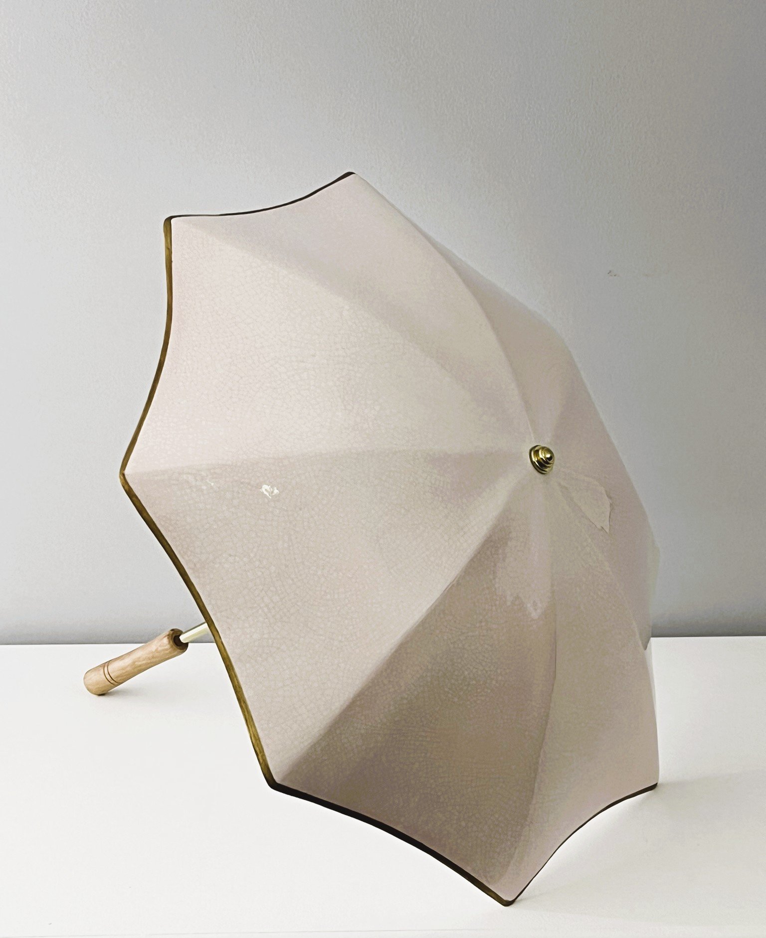 Large cream ceramic umbrella with a crazed pink glaze pattern through it and gold edging