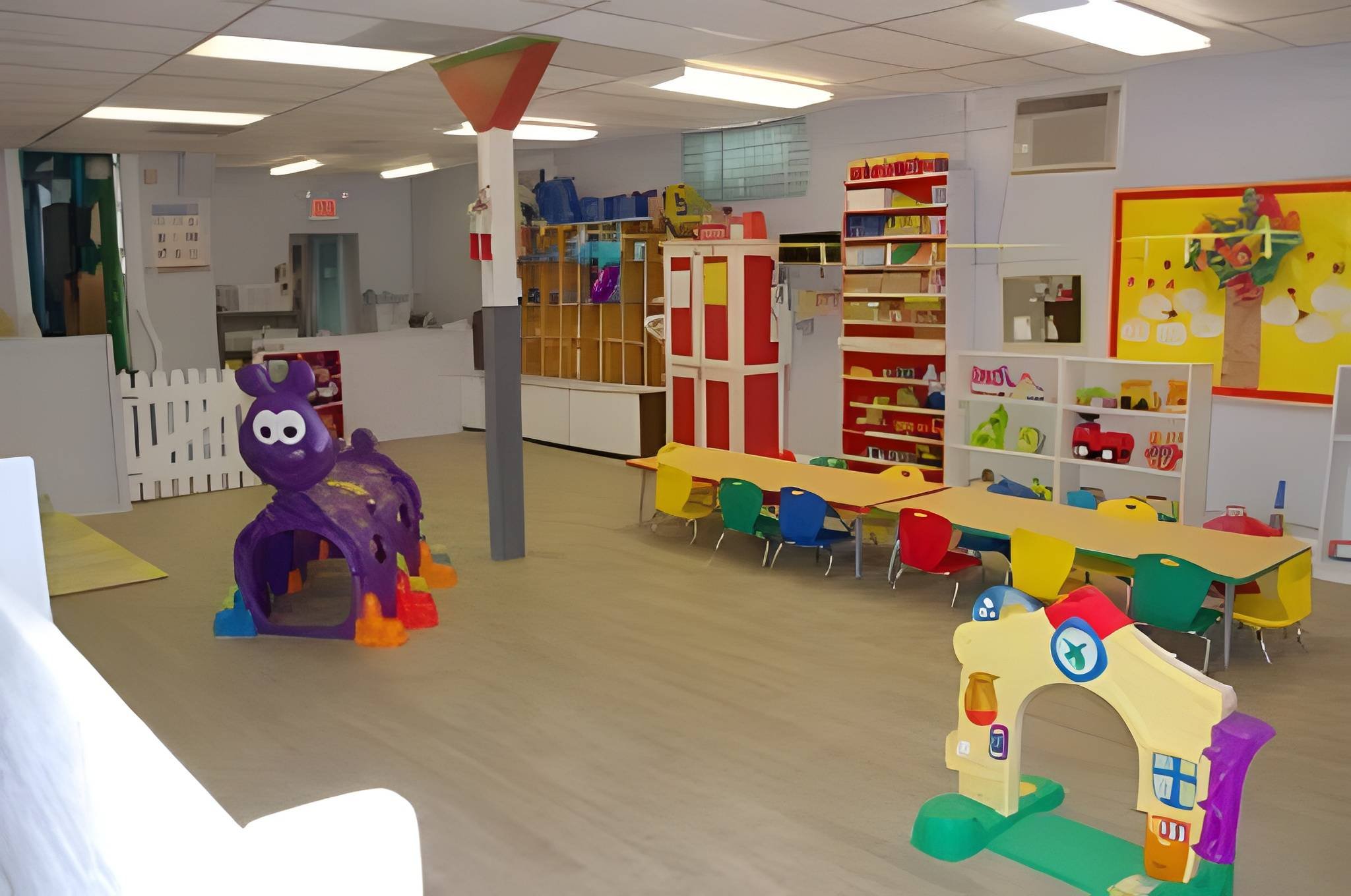 Empty preschool classroom with colorful furniture, shelves filled with toys and books, and playful decorations.
