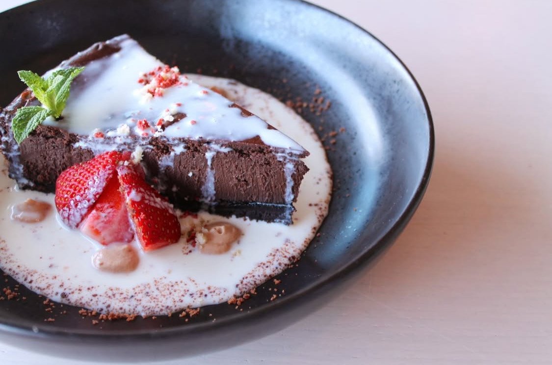 Tarta de chocolate con chocolate blanco, fresas, menta y polvo de cacao en un plato negro.