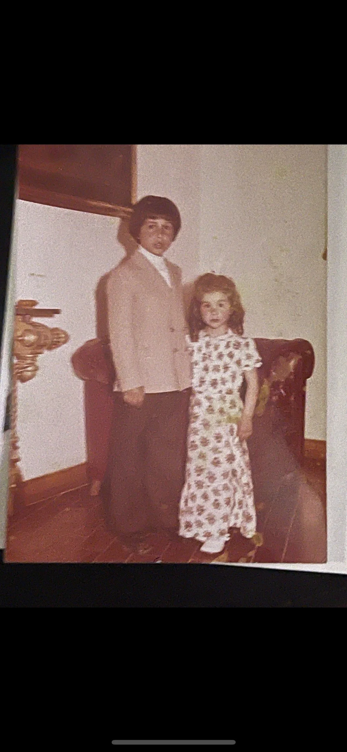 Una fotografía antigua de dos niños, un chico y una chica, posando dentro de una casa. El chico lleva una americana gris y pantalones oscuros, mientras que la chica lleva un vestido largo con un estampado floral. Son los dueños del restaurante.