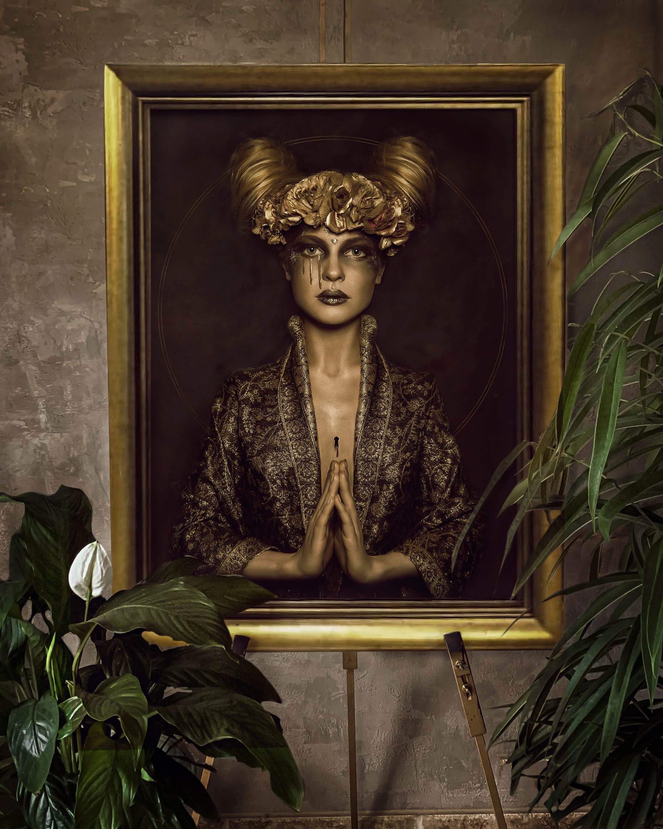 A woman with elaborate hair and makeup, dressed in a gold patterned blazer, is depicted in a framed portrait with her hands pressed together in a prayer-like gesture, surrounded by green plants.