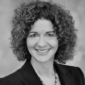 Black and white portrait of a woman with curly hair smiling, wearing a blazer