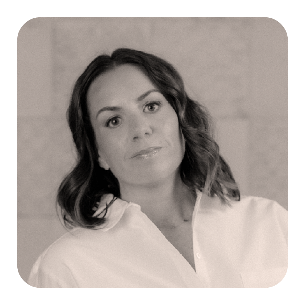 A woman with shoulder-length wavy hair wearing a white button-up shirt, looking directly at the camera with a neutral expression.