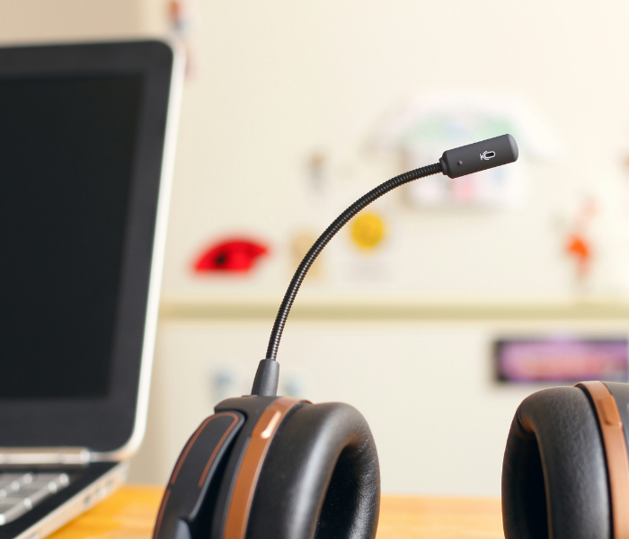 Close-up of a headset with a flexible microphone arm on a desk, with a partially visible laptop in the background.