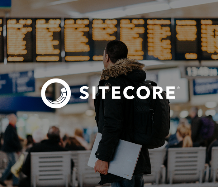 A traveler with a laptop standing in an airport terminal, looking at the departure or arrival screens above.