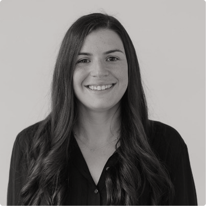 Black and white portrait of a young woman with long, wavy hair, smiling, wearing a dark blouse, against a plain light background.