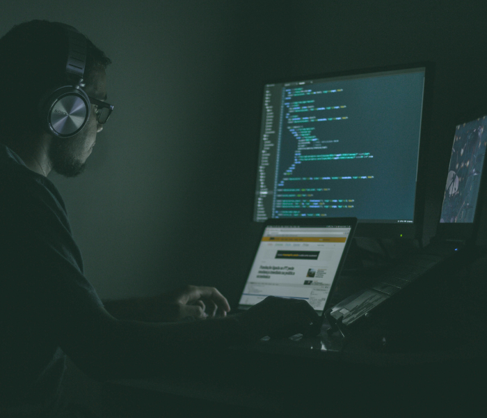 Man with headphones working on a computer with multiple screens showing code and web page.