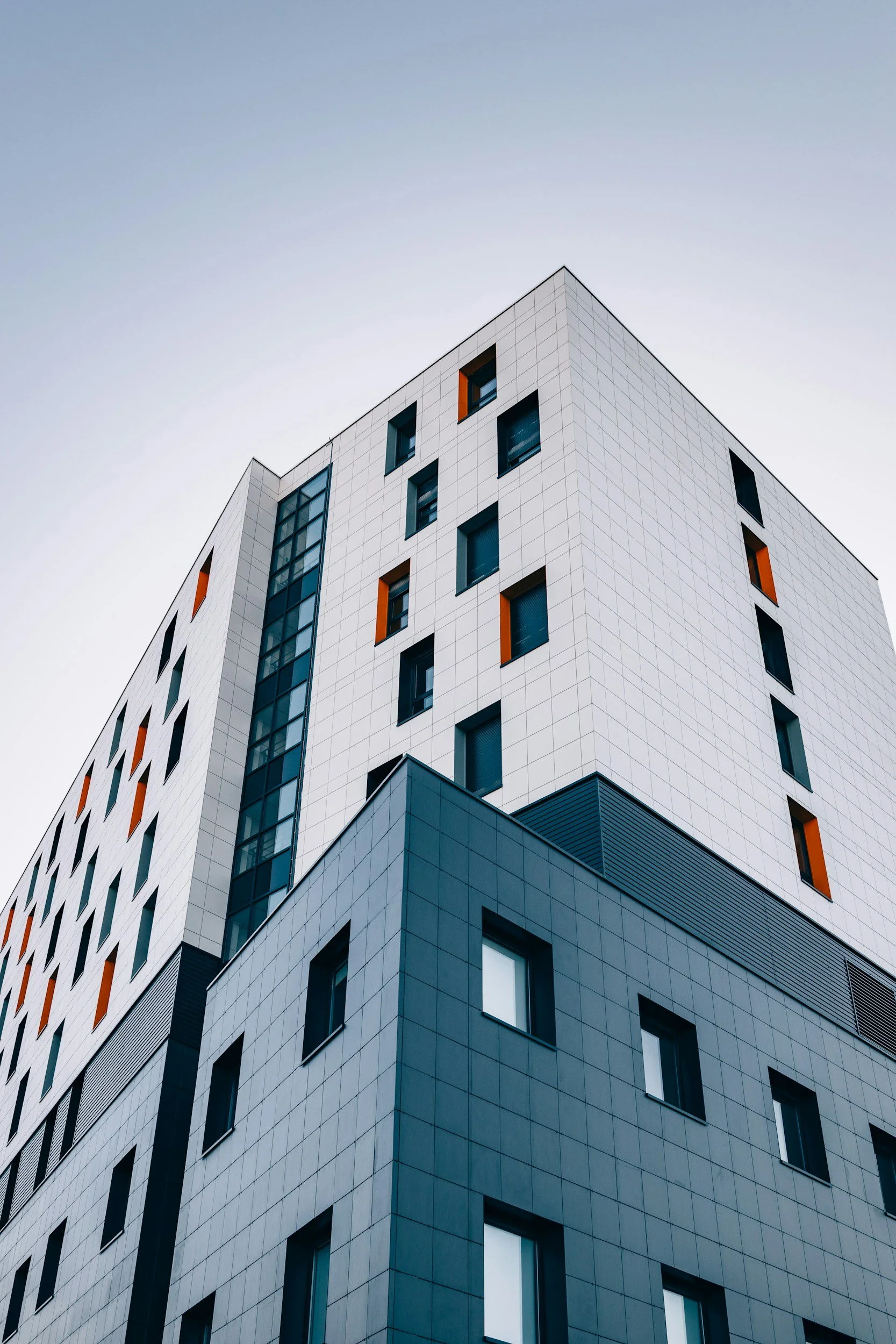 Edificio moderno con facciata bianca e finestra nera, alcune finestre hanno dettagli arancioni.