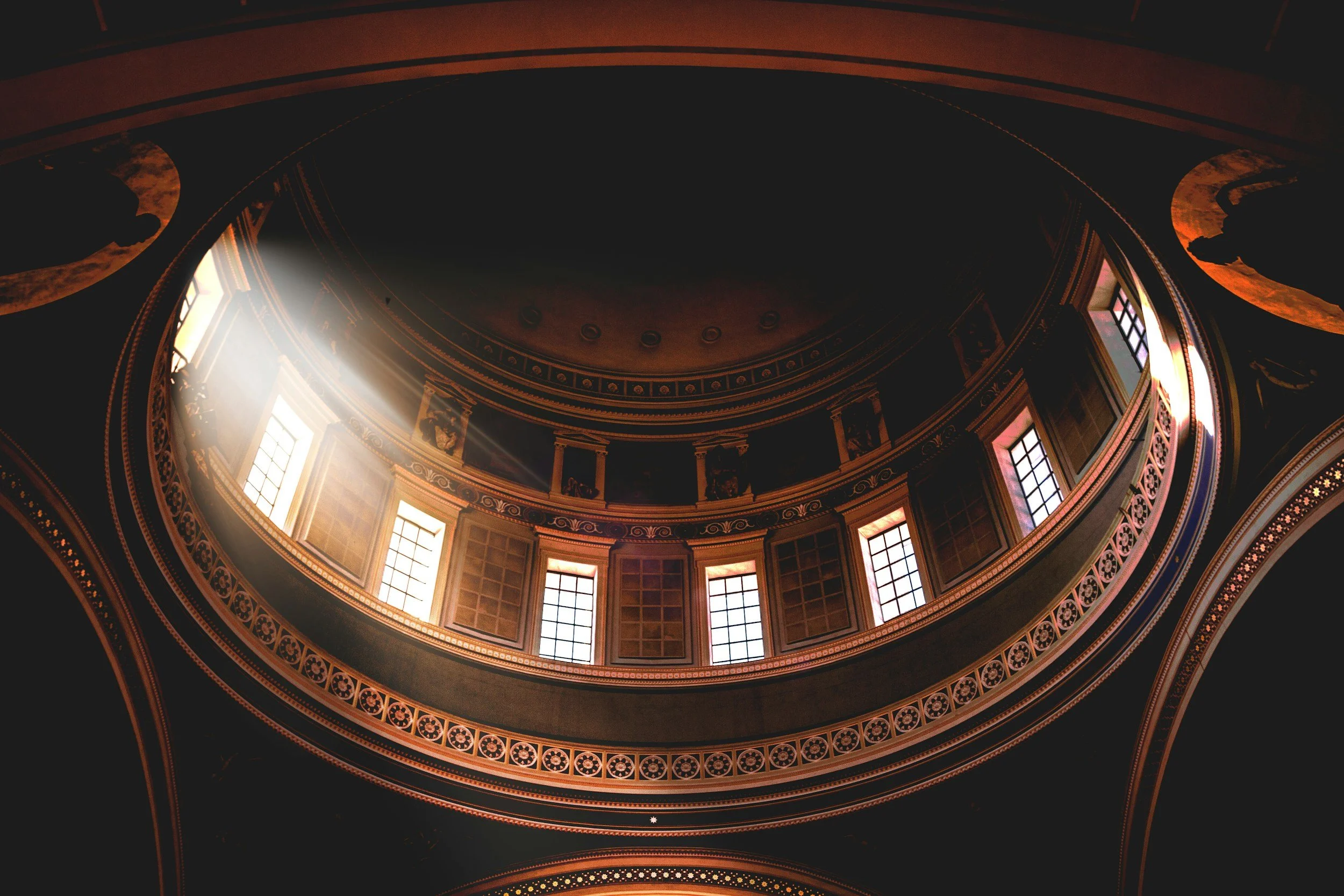 Interno di un teatro con finestre che lasciano entrare la luce e decorazioni dorate lungo le pareti e il soffitto, con un'atmosfera storica e elegante.