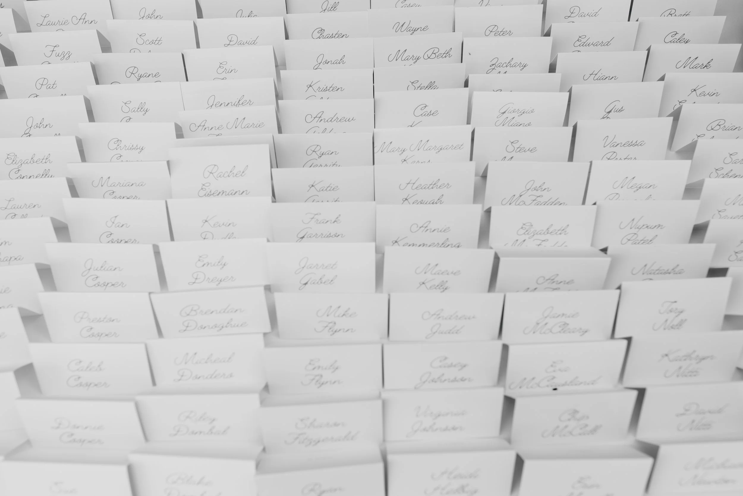 Multiple white paper name tags with handwritten names arranged in rows and columns.