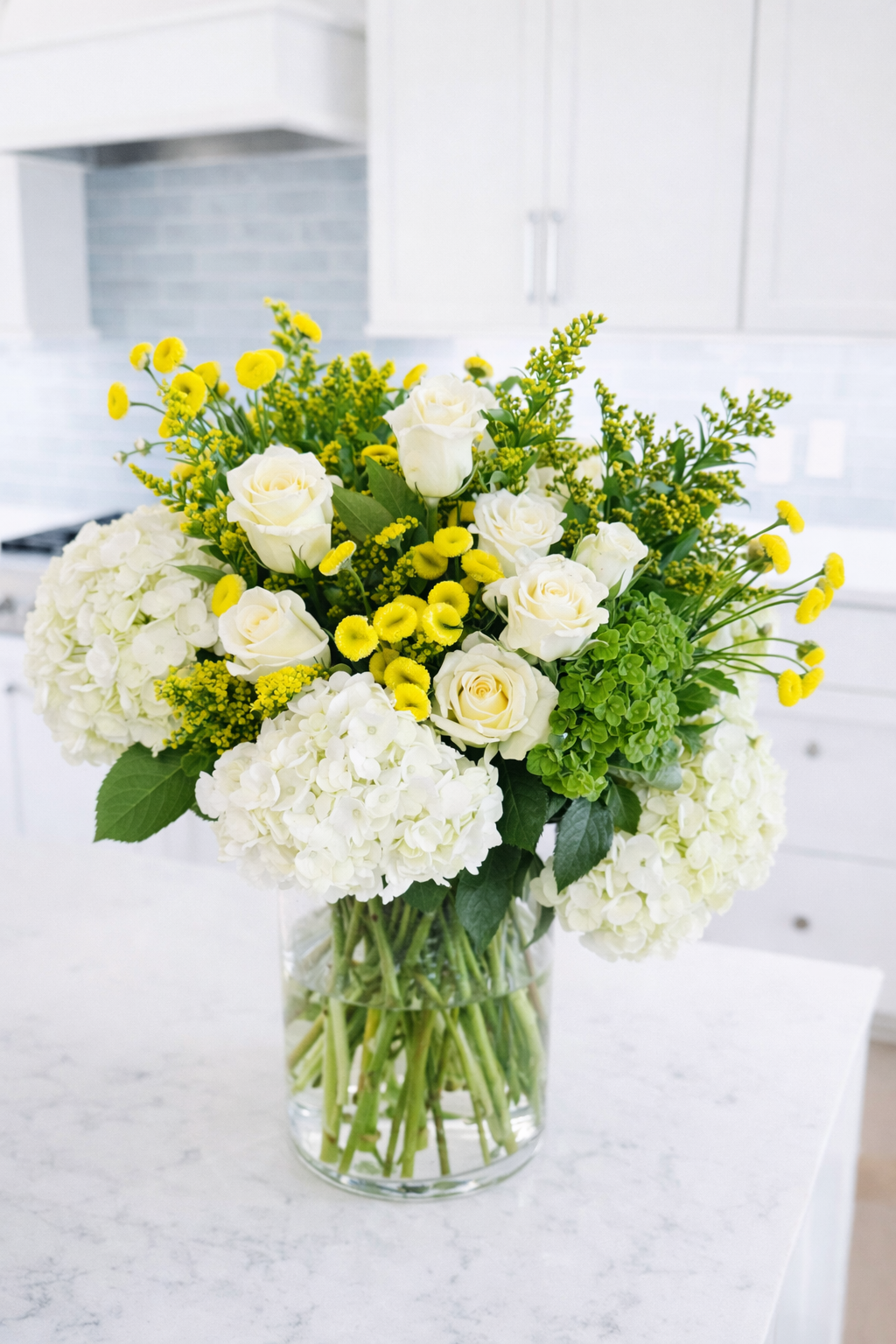 Vase of white roses, hydrangeas, and yellow flowers on a white kitchen counter.