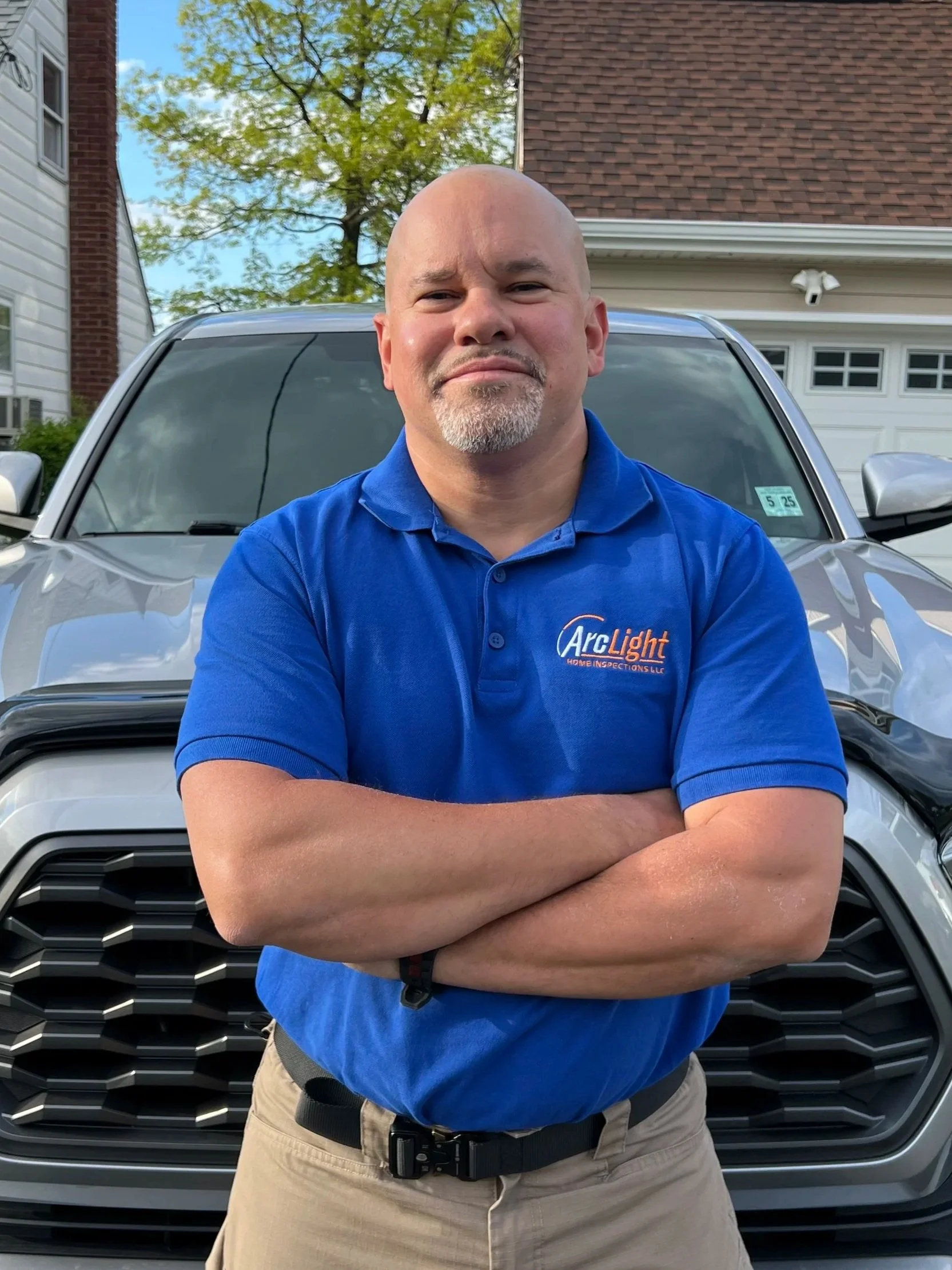 James Morales from Arc light home inspections performing a residential home inspection stands with arms crossed in front of a silver SUV in a residential driveway.