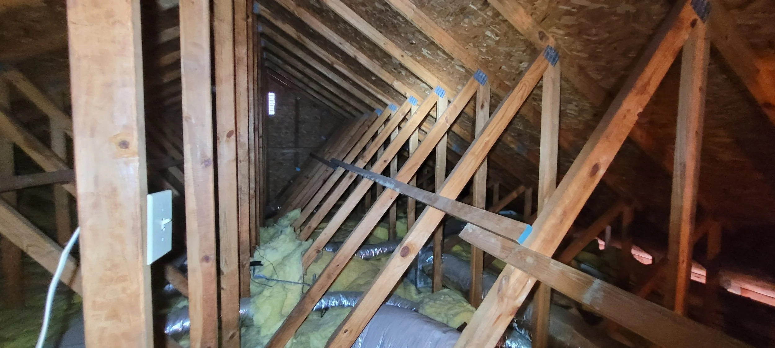 Construction inside an attic showing exposed wooden framing and insulation on the floor. Arc Light Home Inspections