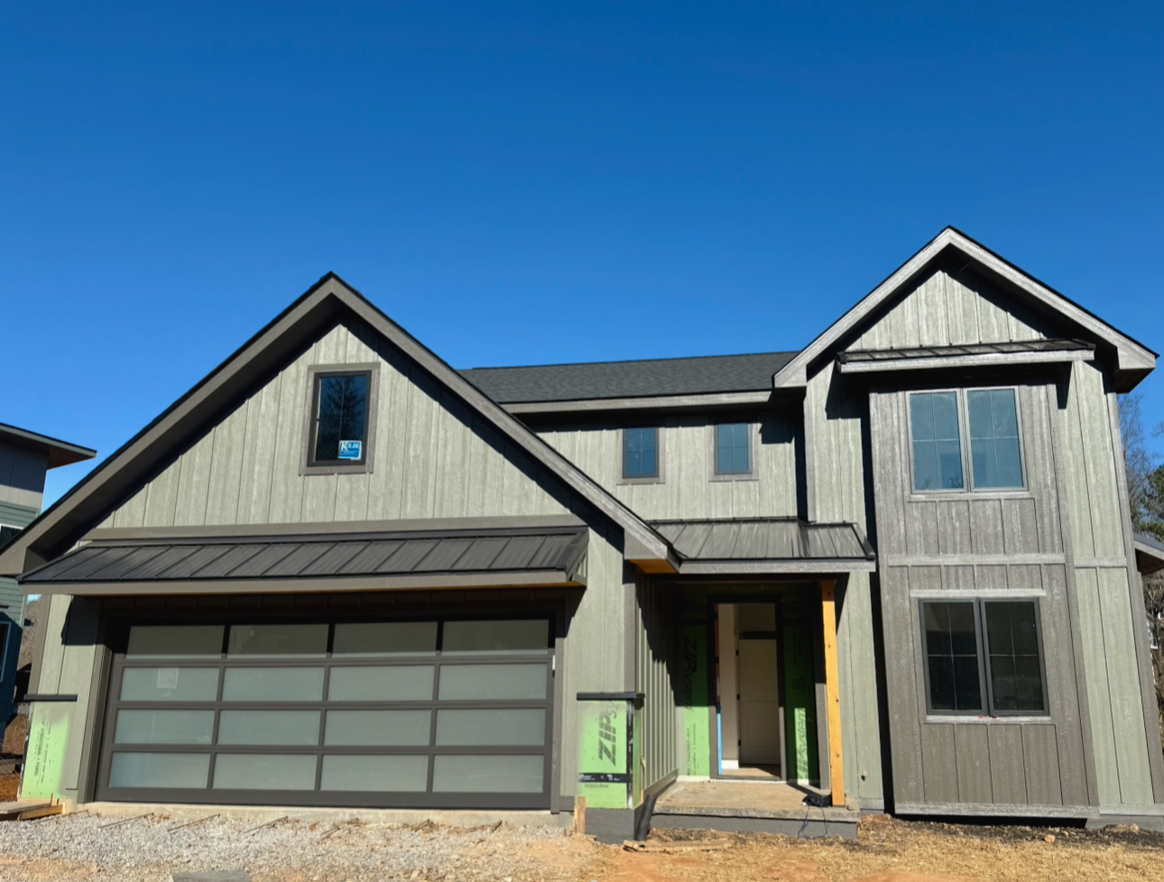 Newly constructed two-story house with gray exterior, garage door, and open front entrance, set against a clear blue sky.