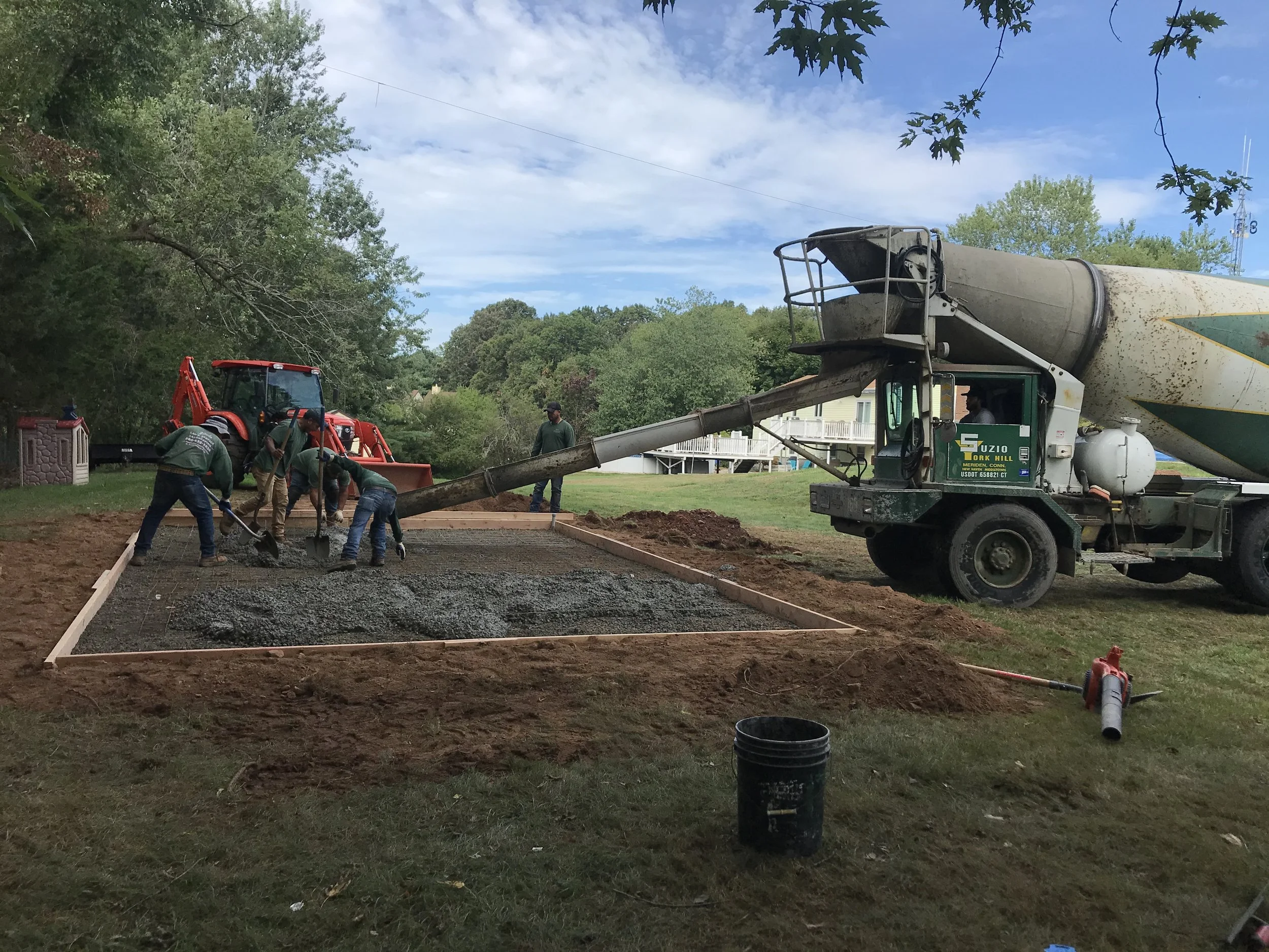 Workers are pouring concrete into a wooden frame to create a new sidewalk or foundation, using a concrete mixer truck 