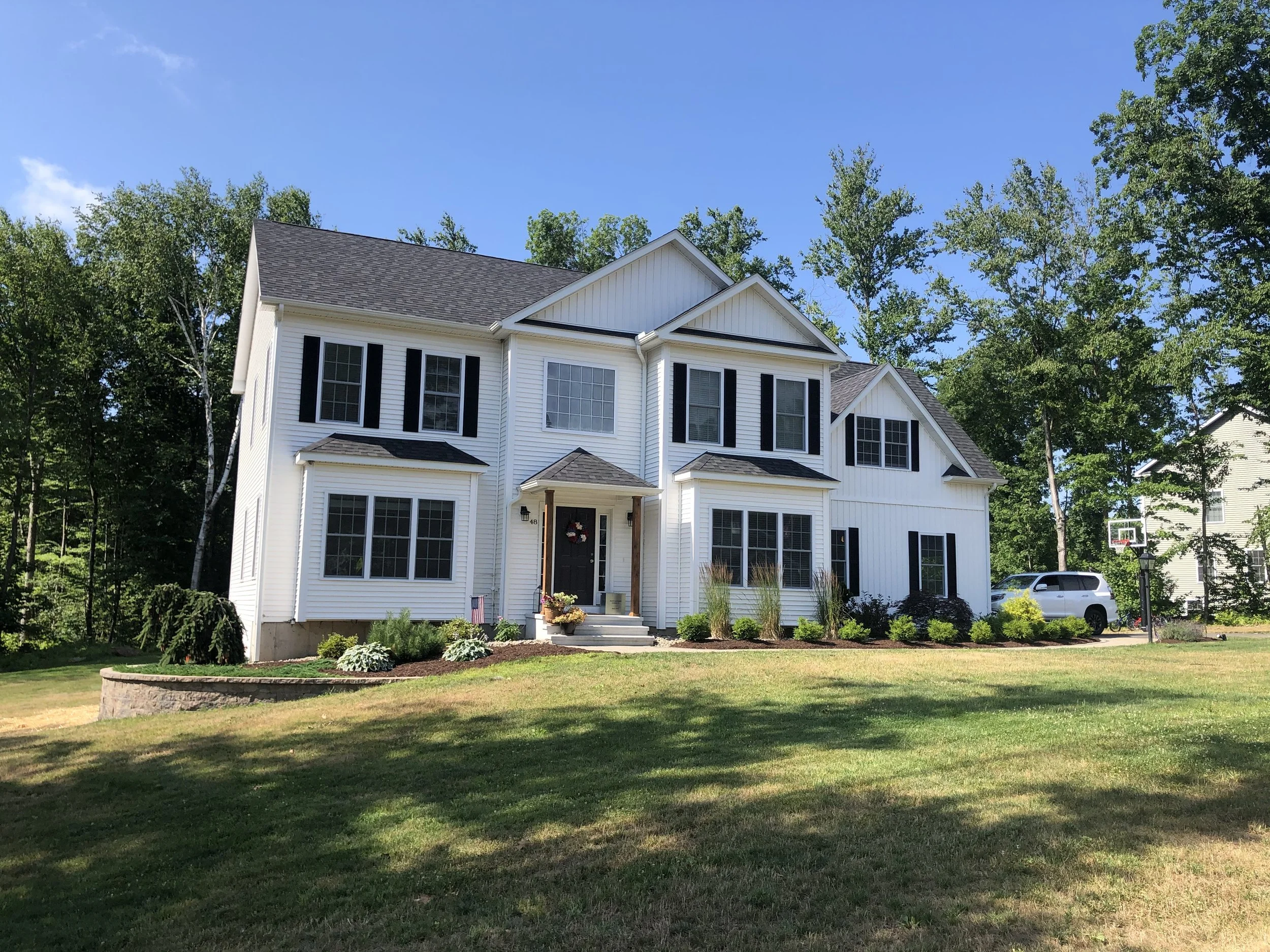Large white two-story house with black shutters and a covered front porch, surrounded by a well-maintained lawn and trees