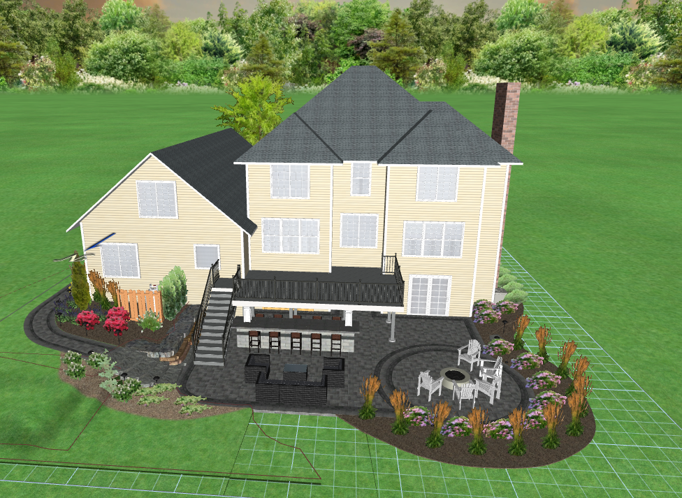 A large beige two-story house with a gray roof and a brick chimney, surrounded by a well-maintained backyard featuring a patio with outdoor furniture, a small garden with flowers, and lush green trees in the background.