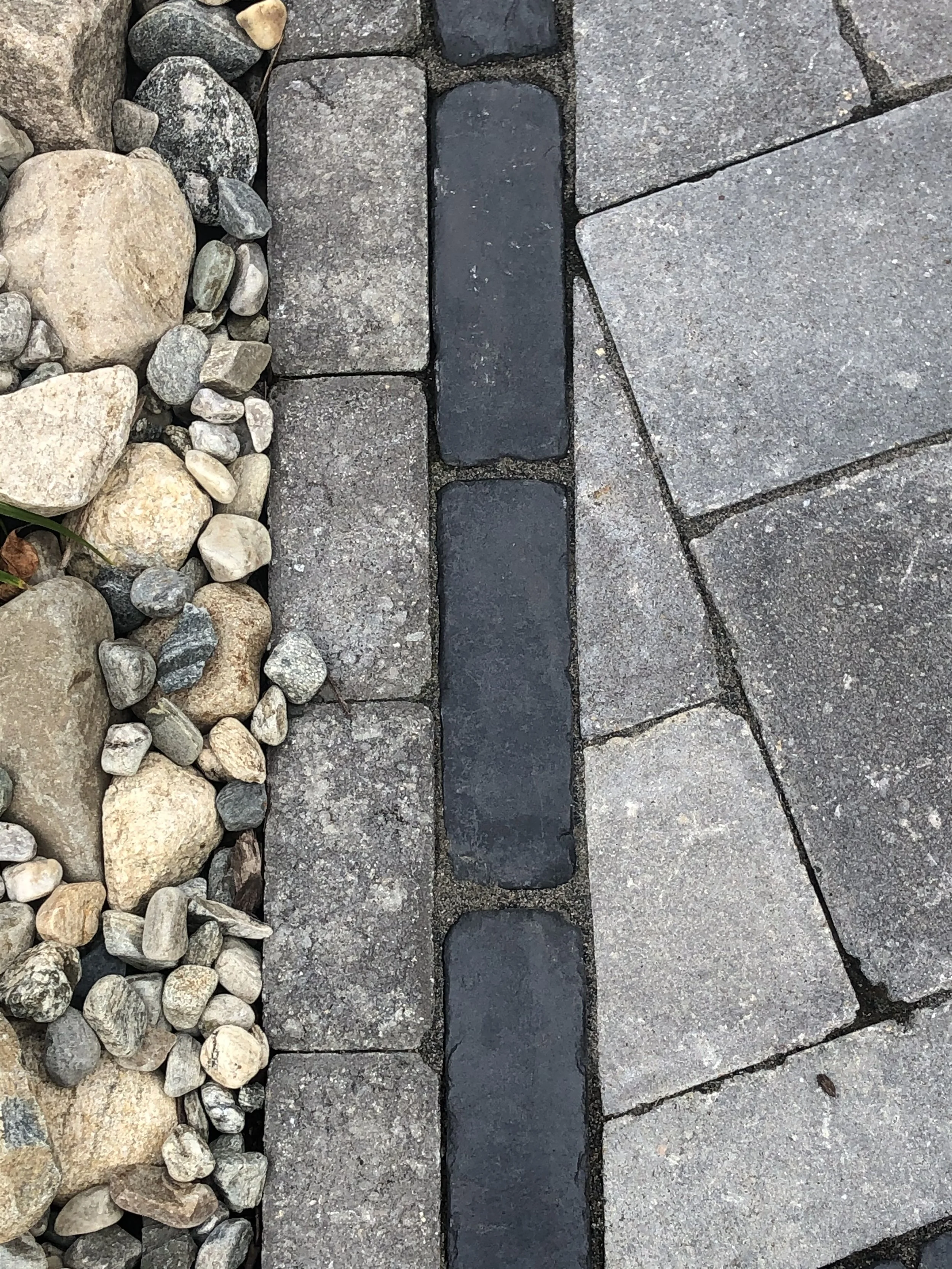 Close-up of a paved pathway with different types of stones, including rocks and bricks, of varying shades of gray and beige.