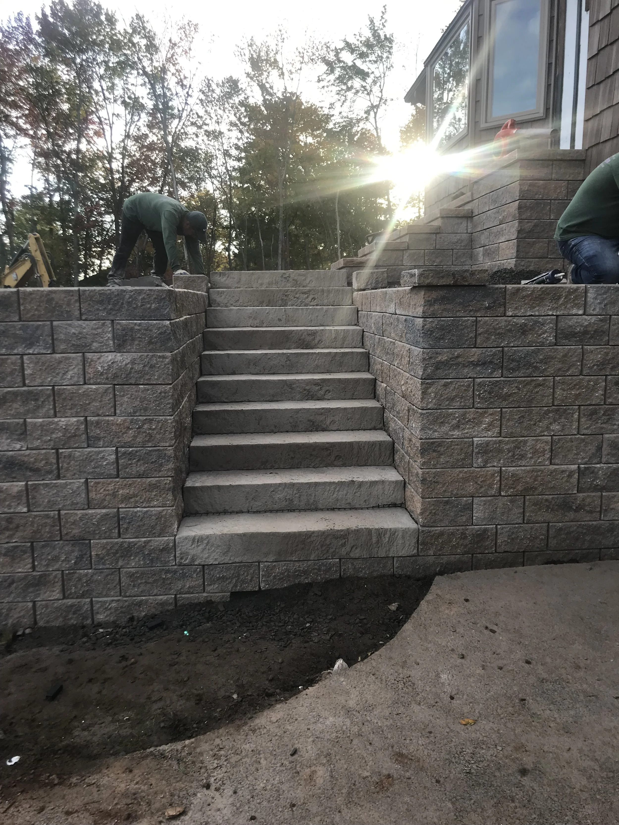 Construction workers installing stone stairs outside a house with a stone retaining wall