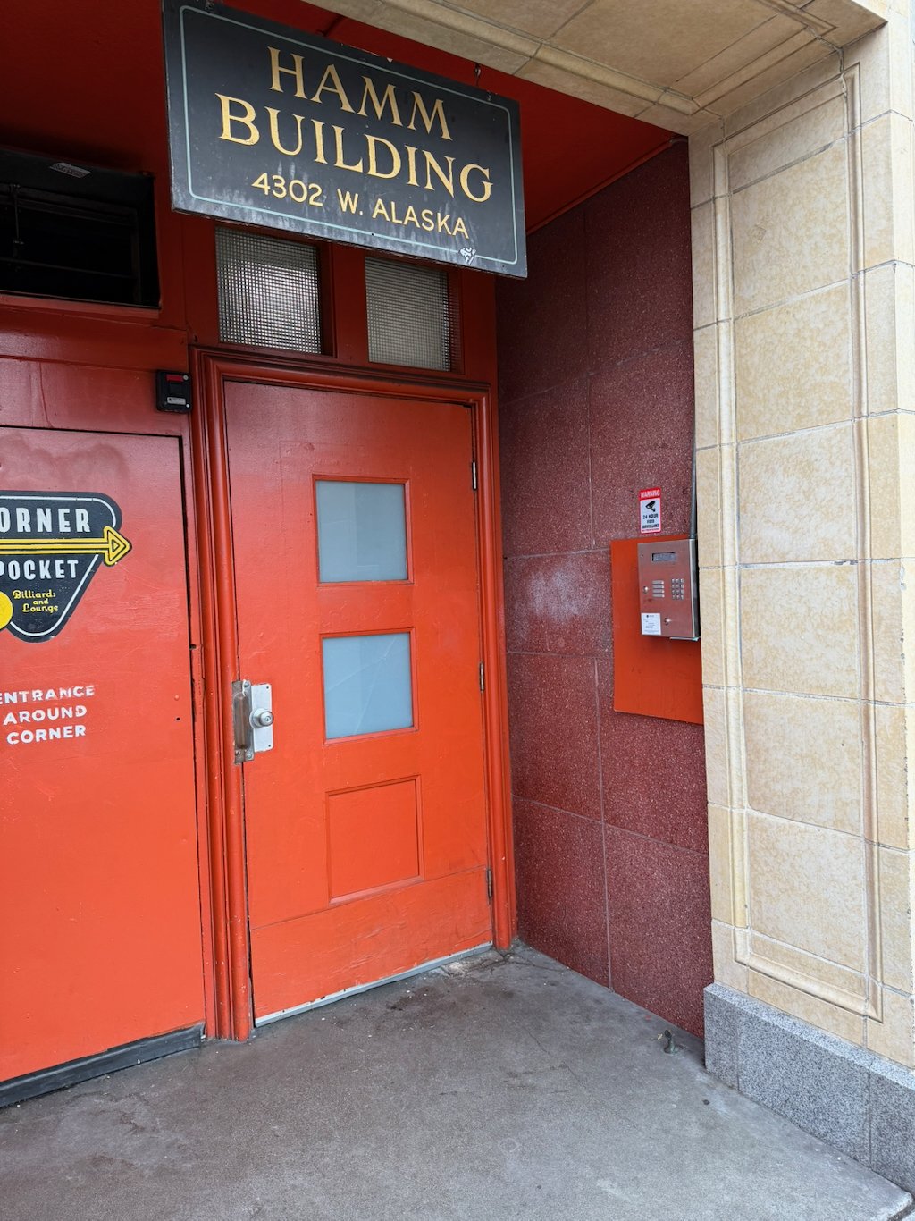 A red door that leads to the stairs to the offices of Just Primary Care, Movement Direct Primary Care, and Fight Night Medicine, which are colocated with Junction Naturopathic Medicine. Also pictured is the sign of the Hamm Building and the call box.