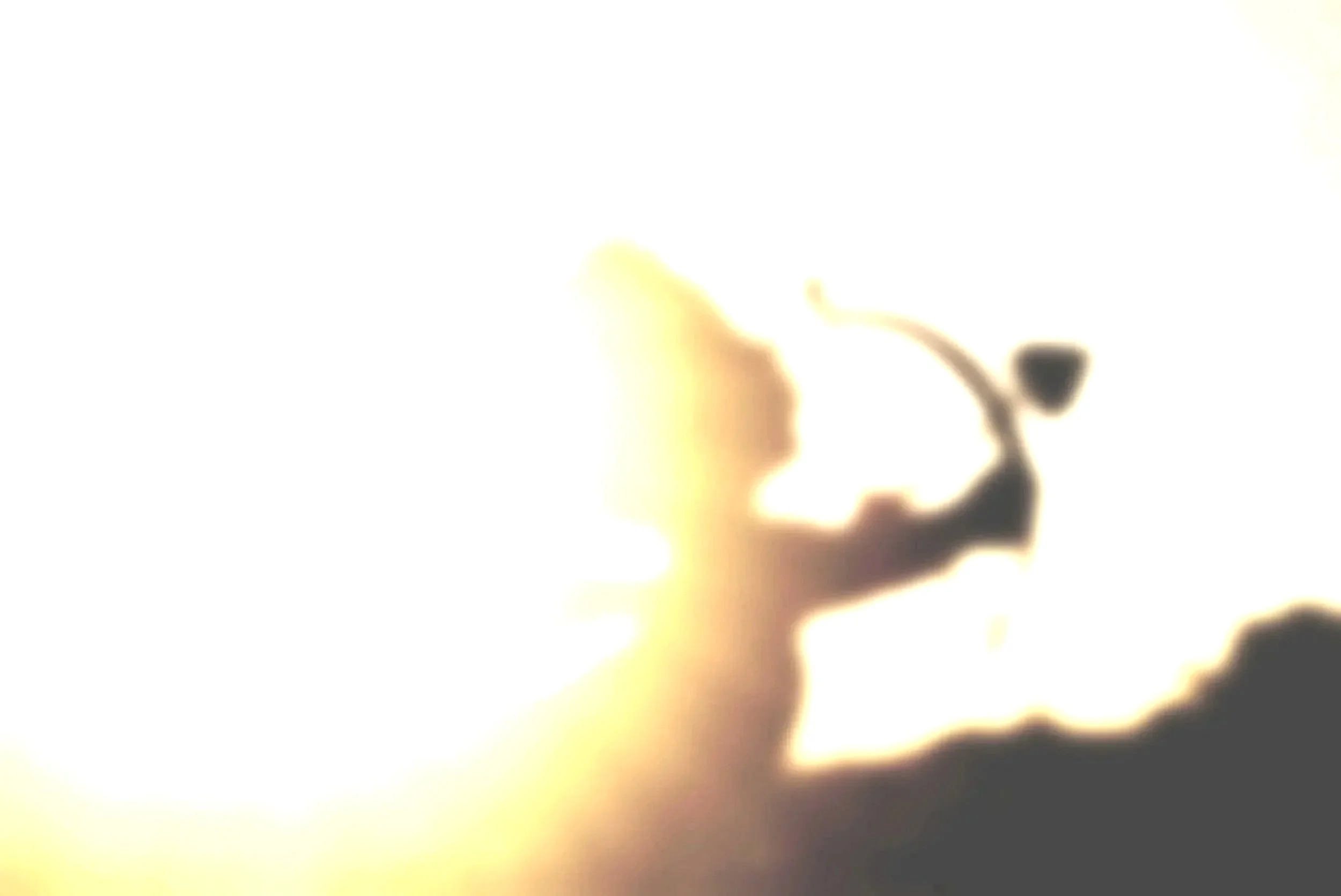 Silhouette of a small angel figure with wings, drawing a bow with an arrow against a bright sunset sky.