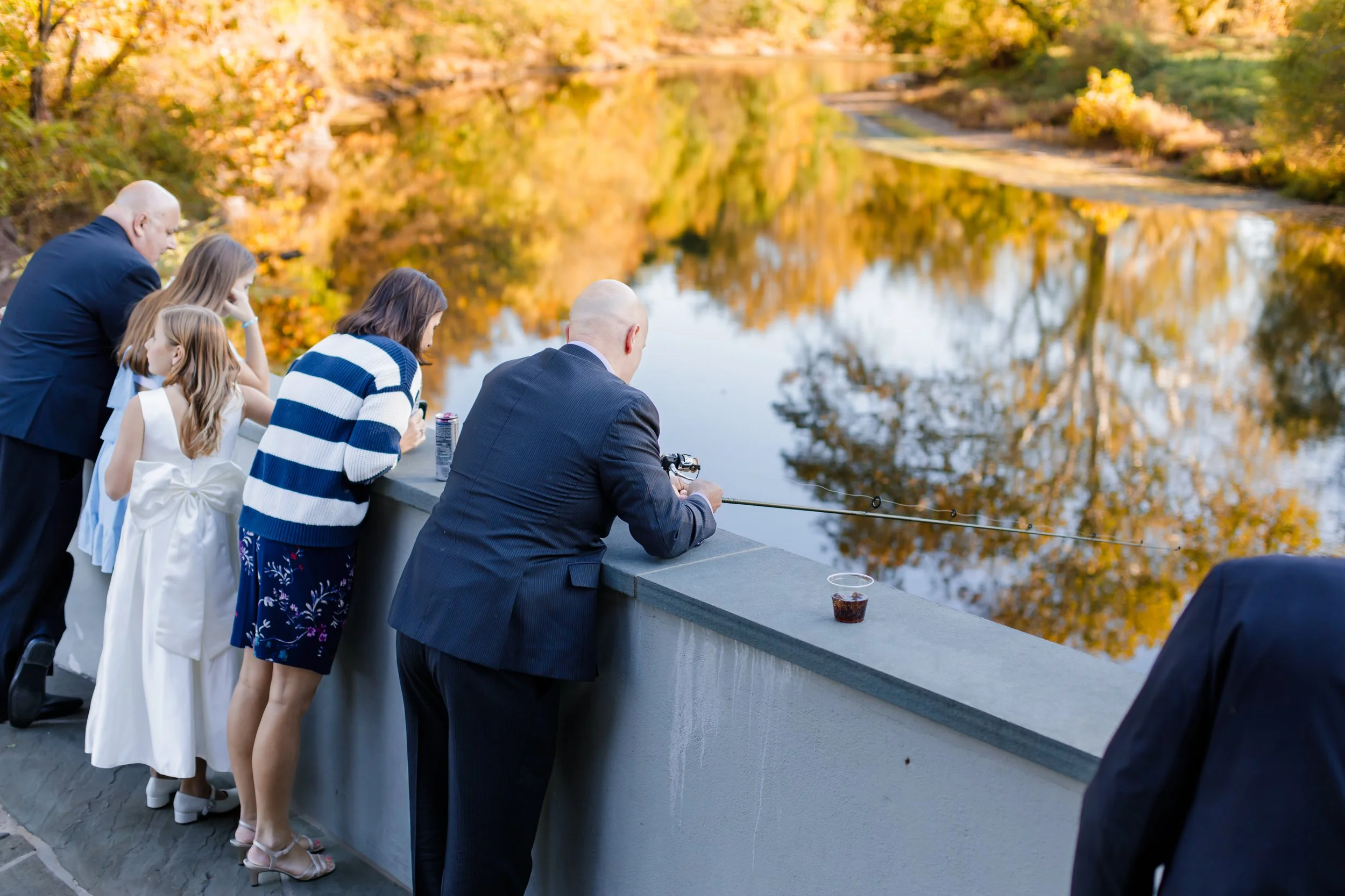 Group of people standing by a railing, fishing in the South Branch Raritan River with autumn trees reflected in the water.