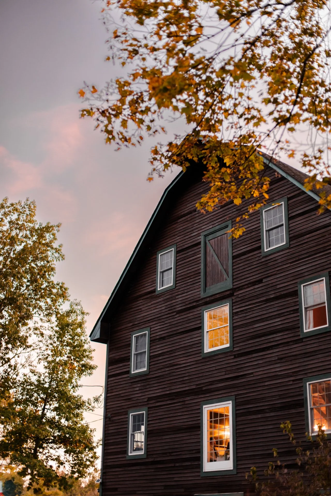 The Neshanic Mill at dusk, in a rural setting, surrounded by trees with autumn leaves.