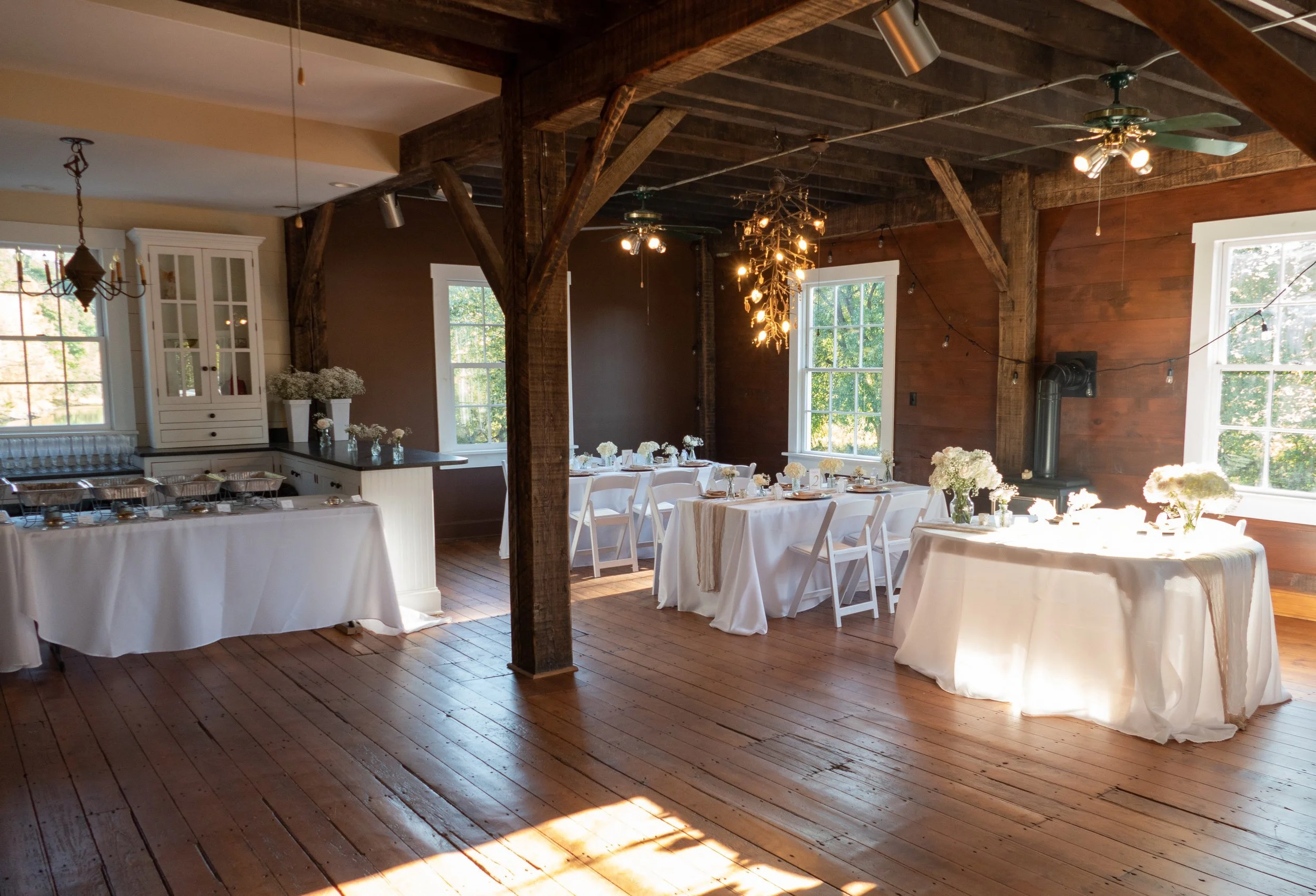 Elegant rustic event space in Central NJ with wooden floors, exposed beams, large windows, and white table settings decorated with flowers.